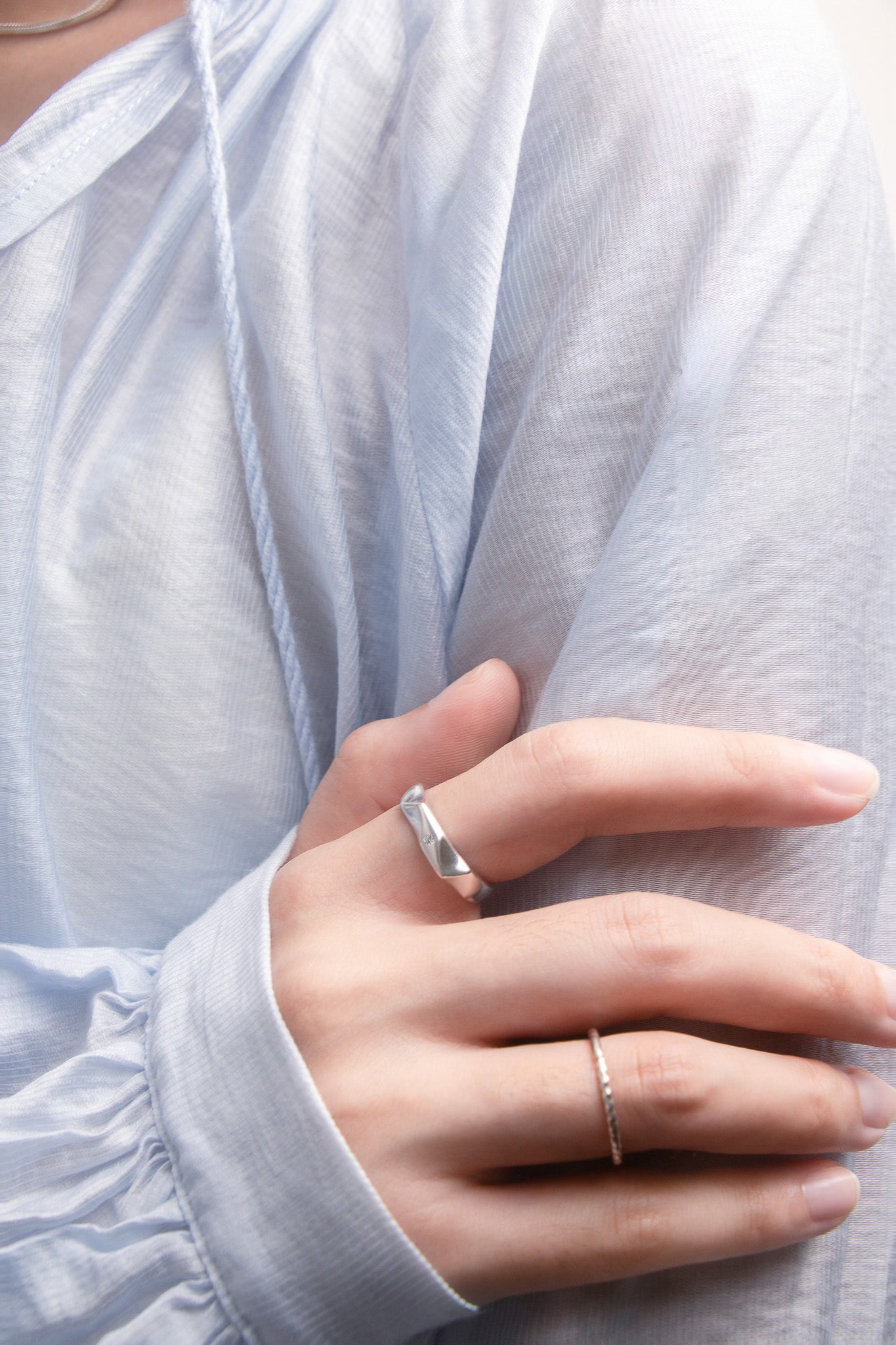 Close-up of a hand wearing two silver rings with a light blue shirt background