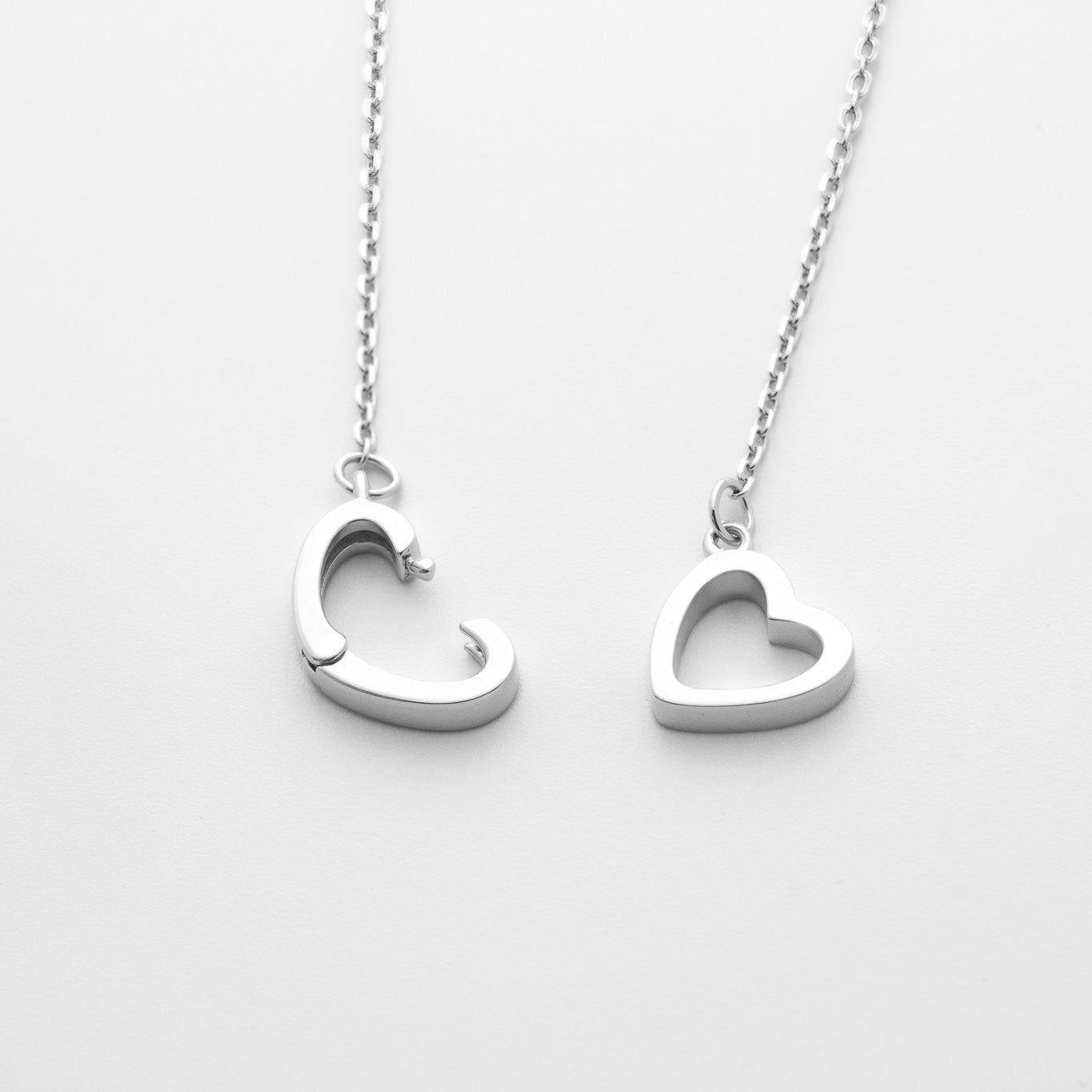 Two silver heart-shaped pendants on a chain against a white background, close-up top down view