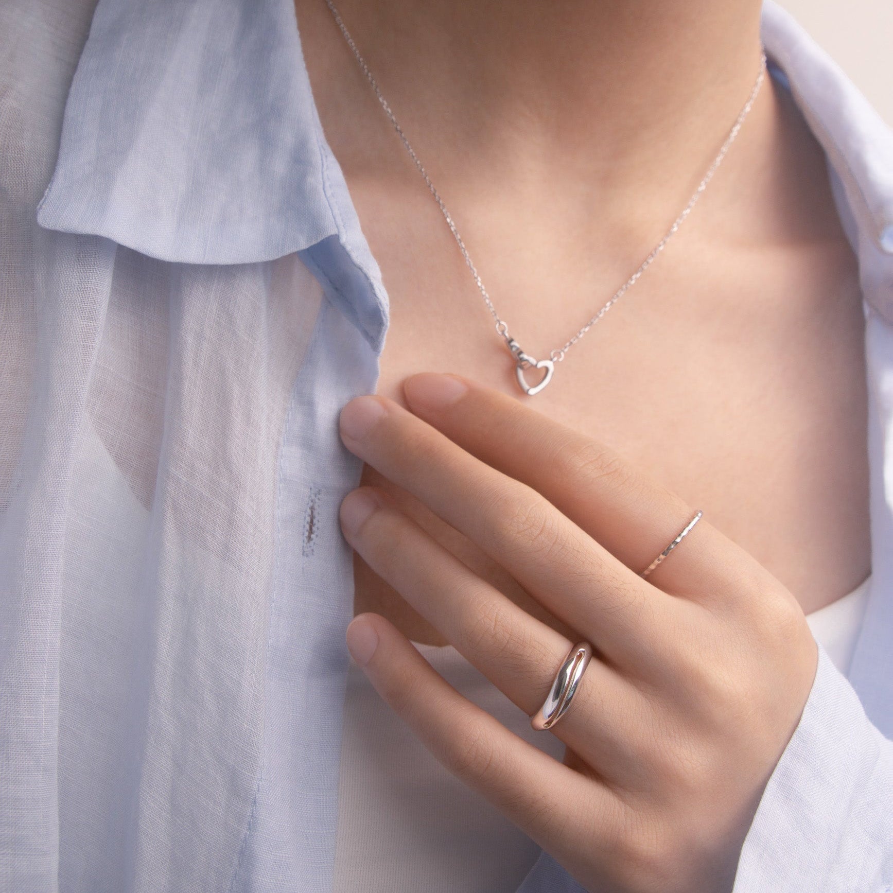 close-up front view of a person wearing a silver necklace and multiple silver ring with a light blue shirt