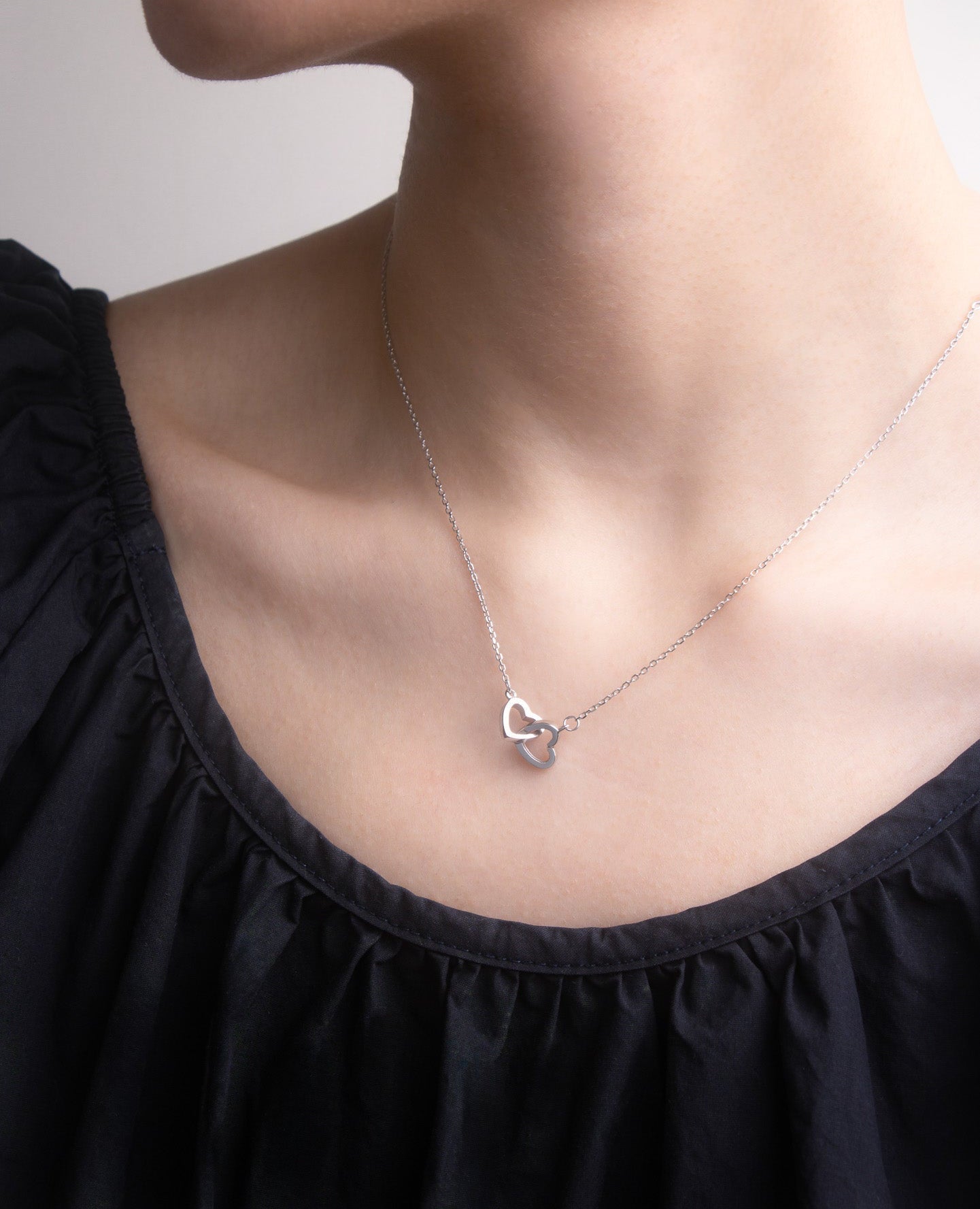 Close-up view of necklace with a heart-shaped pendant worn by a person in a black top.