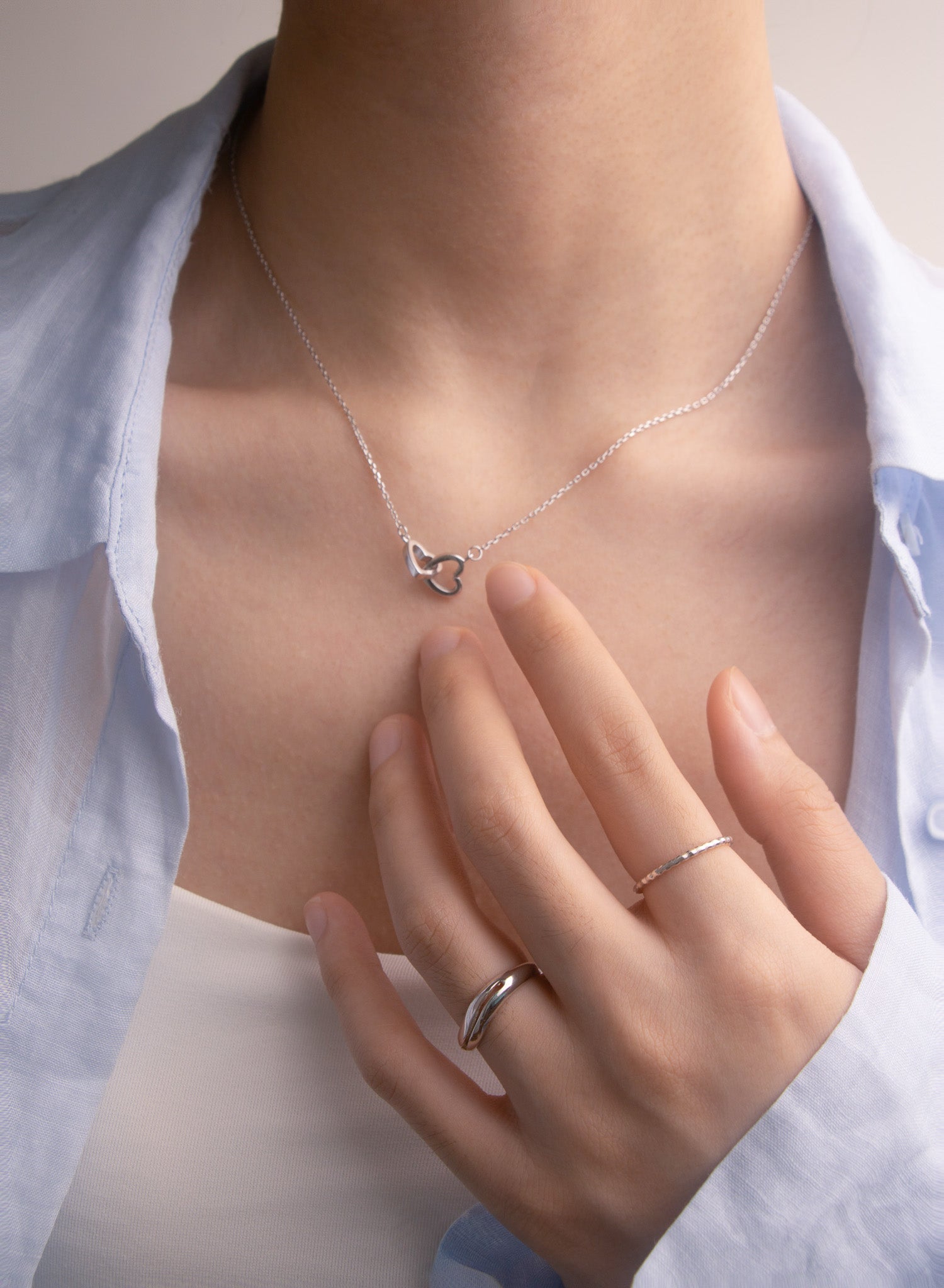 Person wearing a silver necklace and two silver rings with a soft focus background