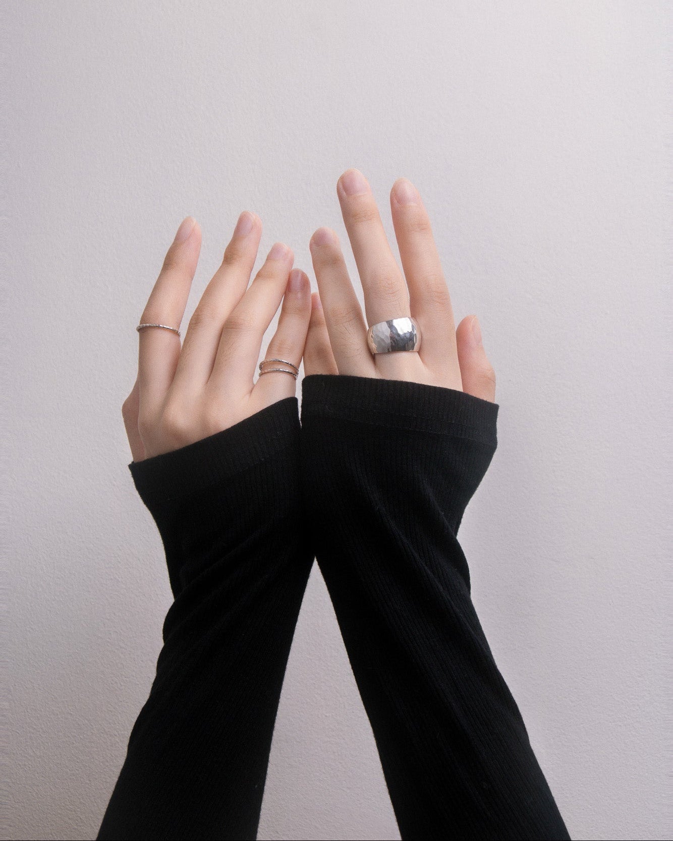 Hands wearing black arm sleeves with silver rings on a plain background, close up front view