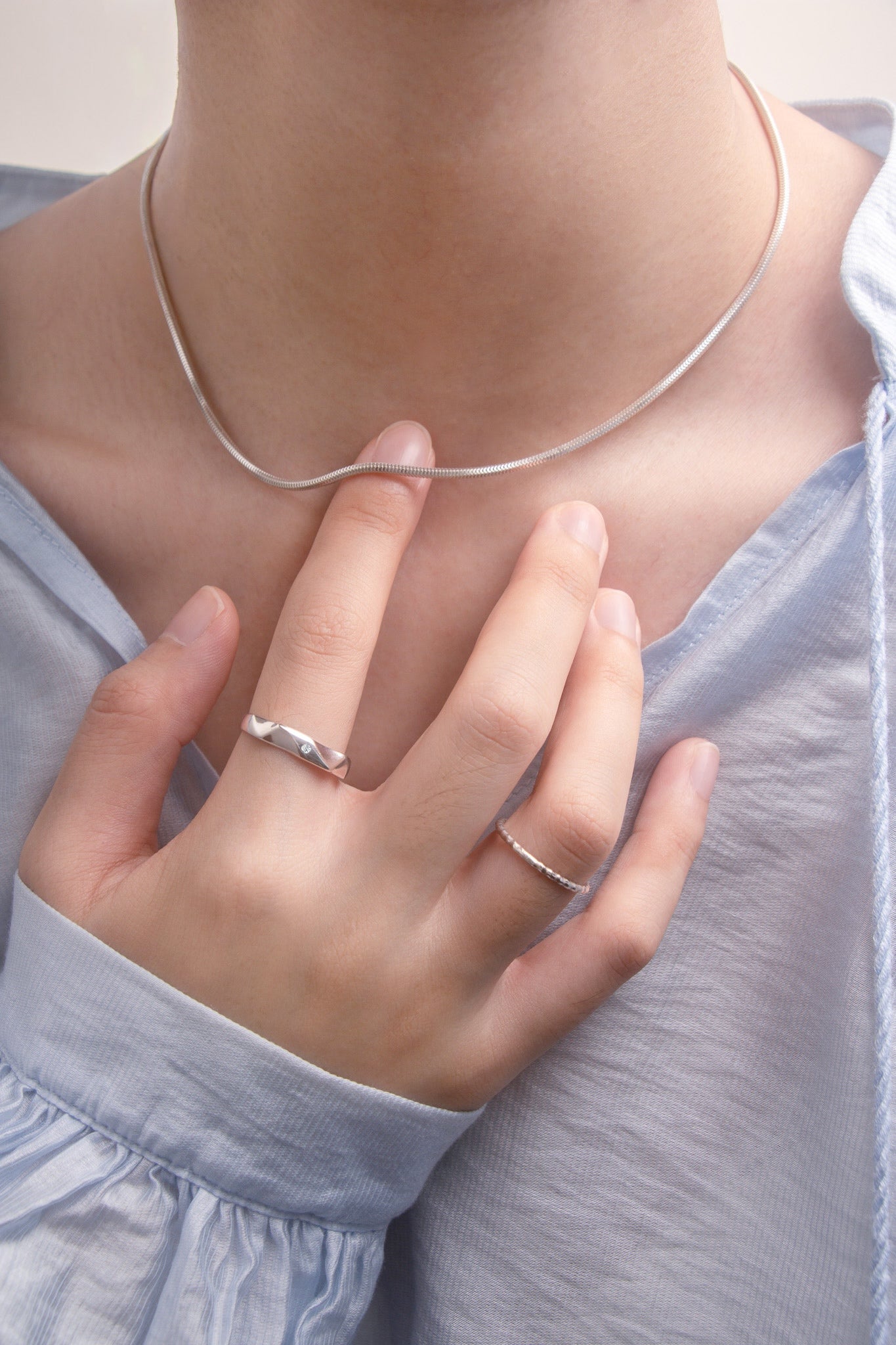 Close-up of a person wearing a silver necklace, ring, on a blurred background. Front view.