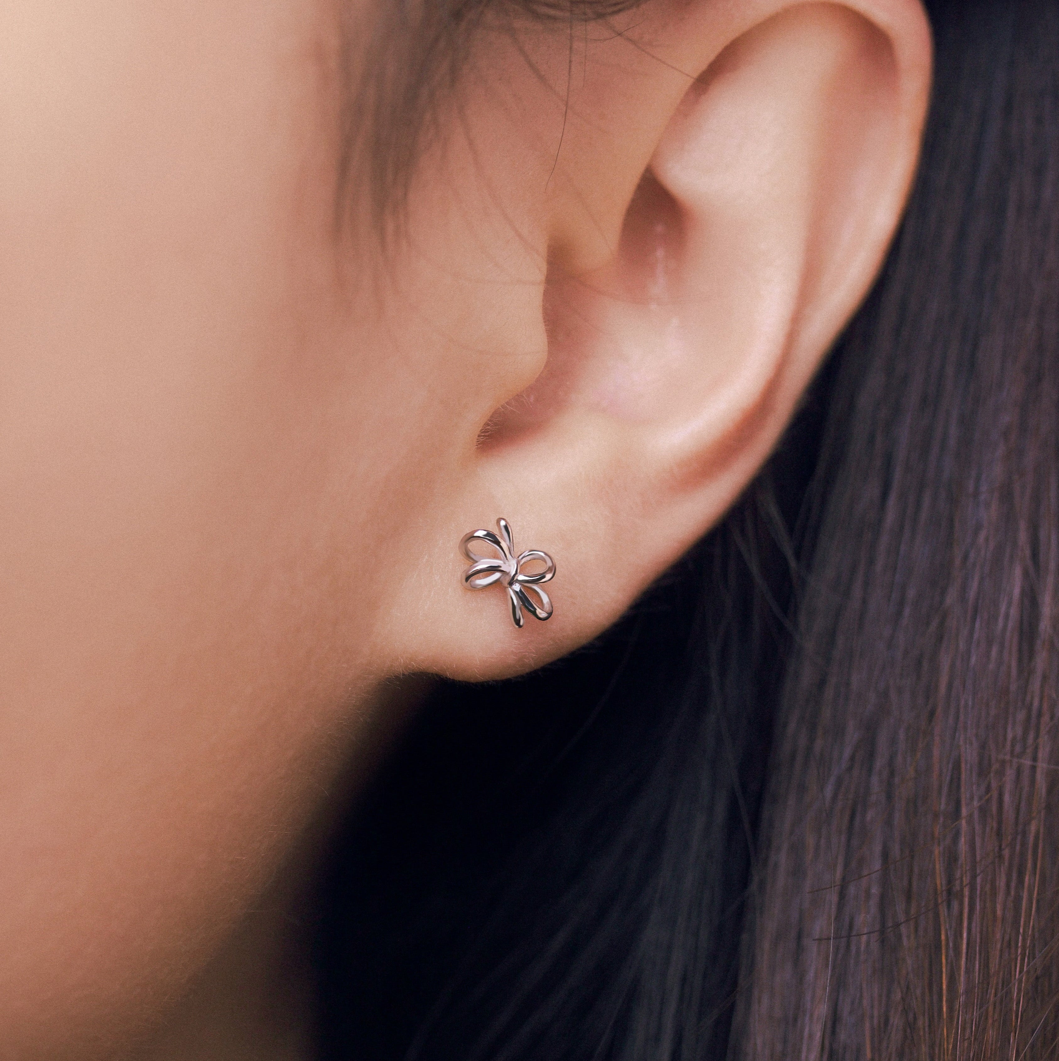 Close-up of an ear wearing a small bow-shaped earring worn on a person's ear