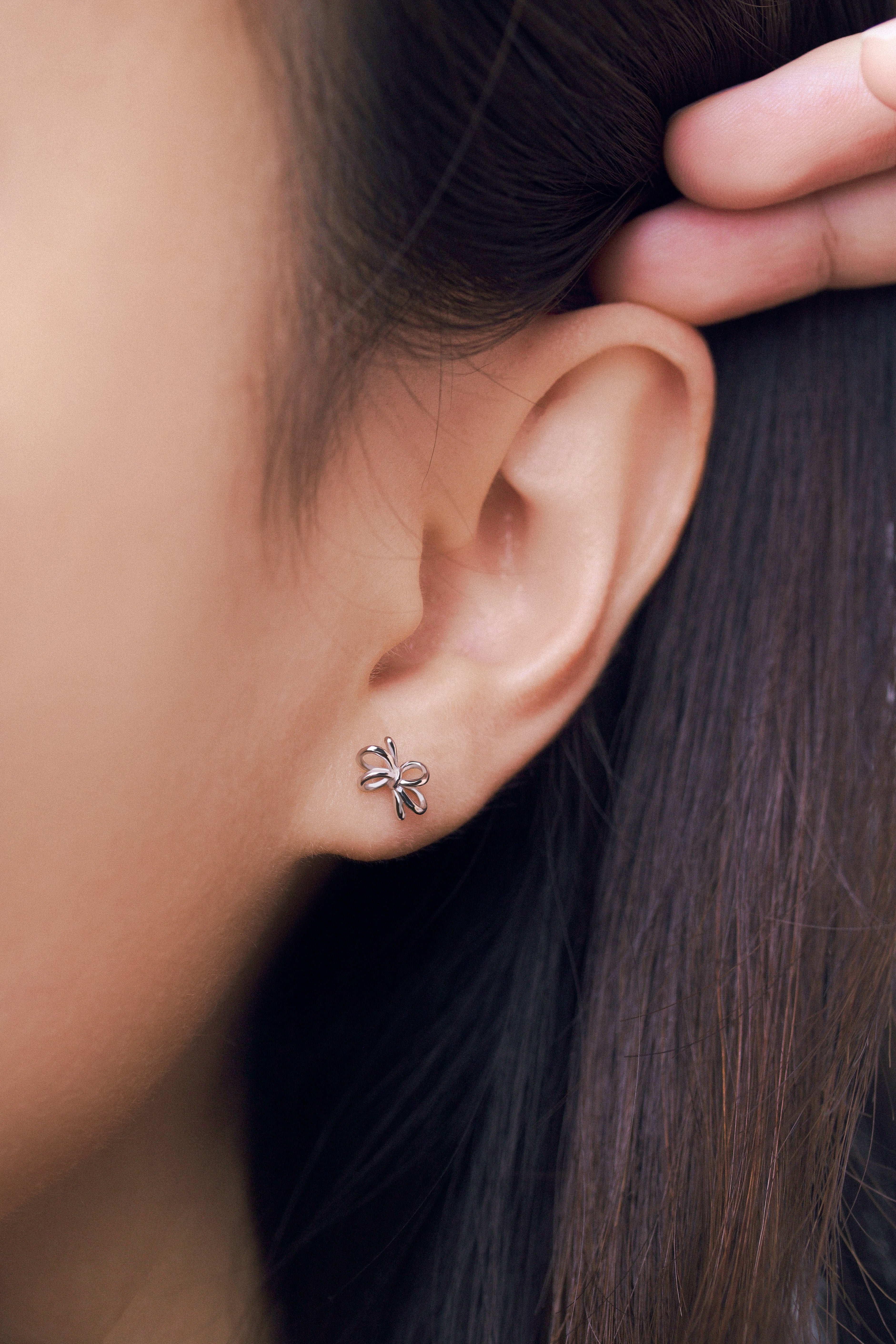 Close-up of an ear wearing a small bow-shaped earring worn on a person's ear