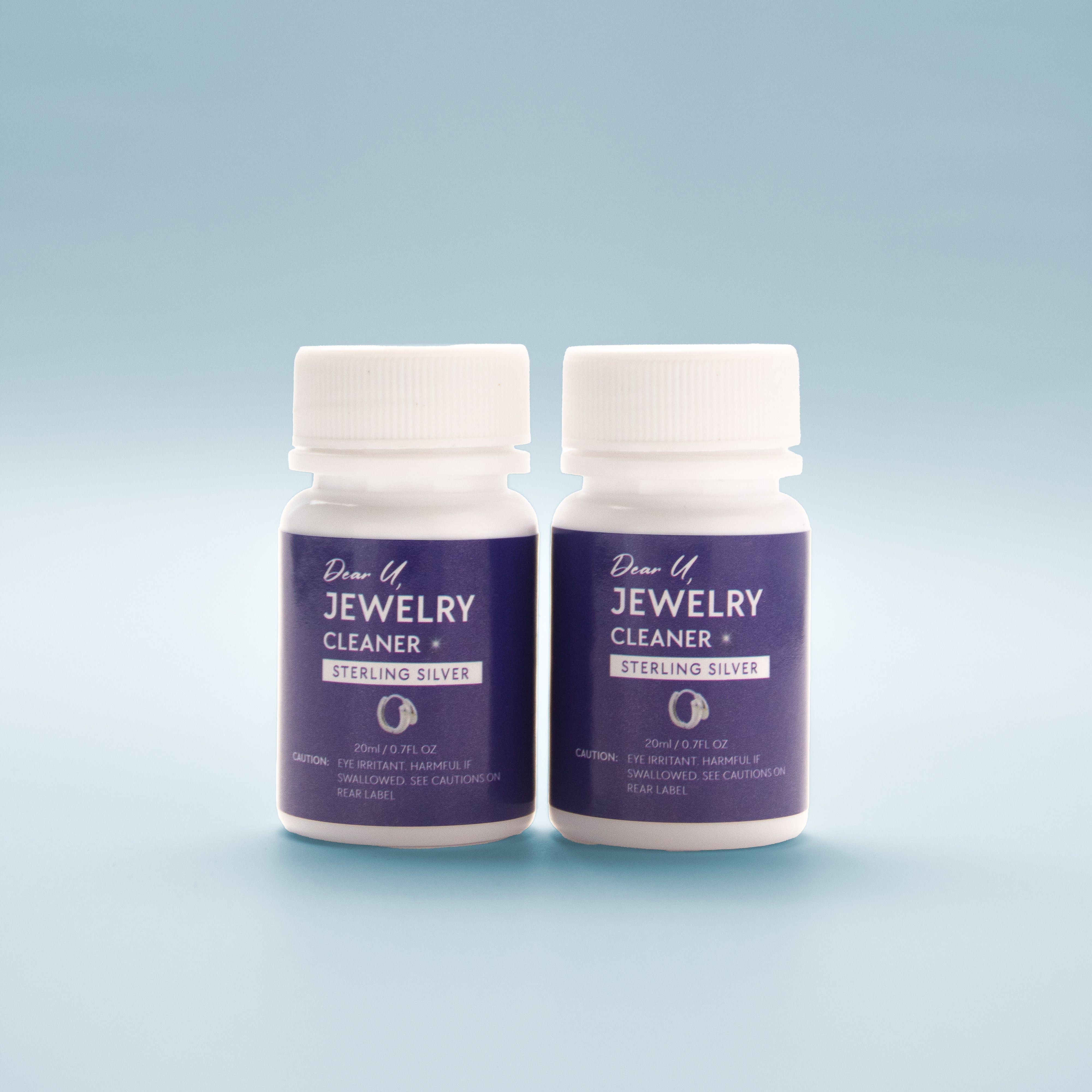 Close-up front view of two bottles of Jewellery Cleaner with blue label on a light blue background