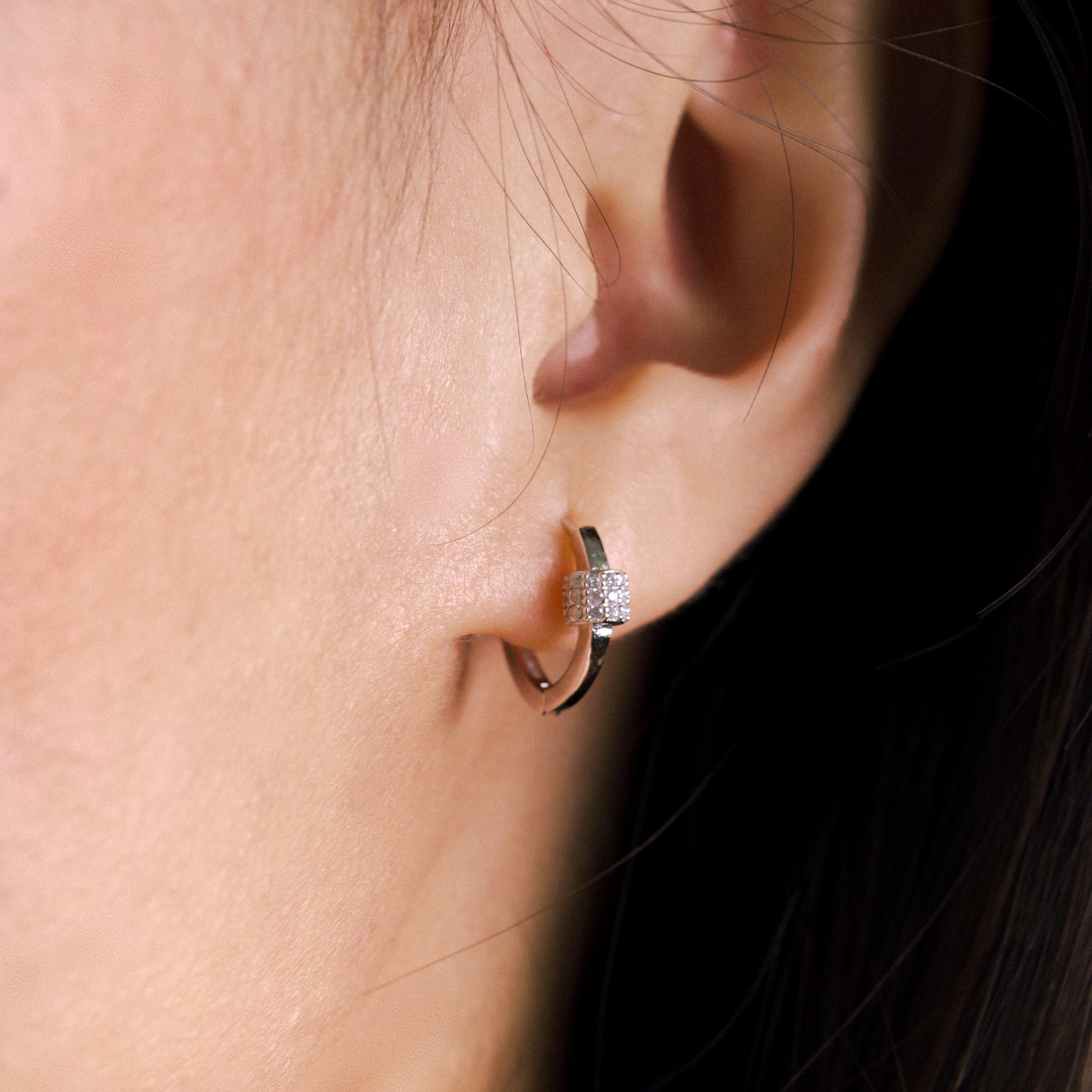 Fine jewellery, silver jewellery, hypoallergenic, tarnish-free, close-up right view of a Silver hoop earrings with embedded stones worn on a person's ear