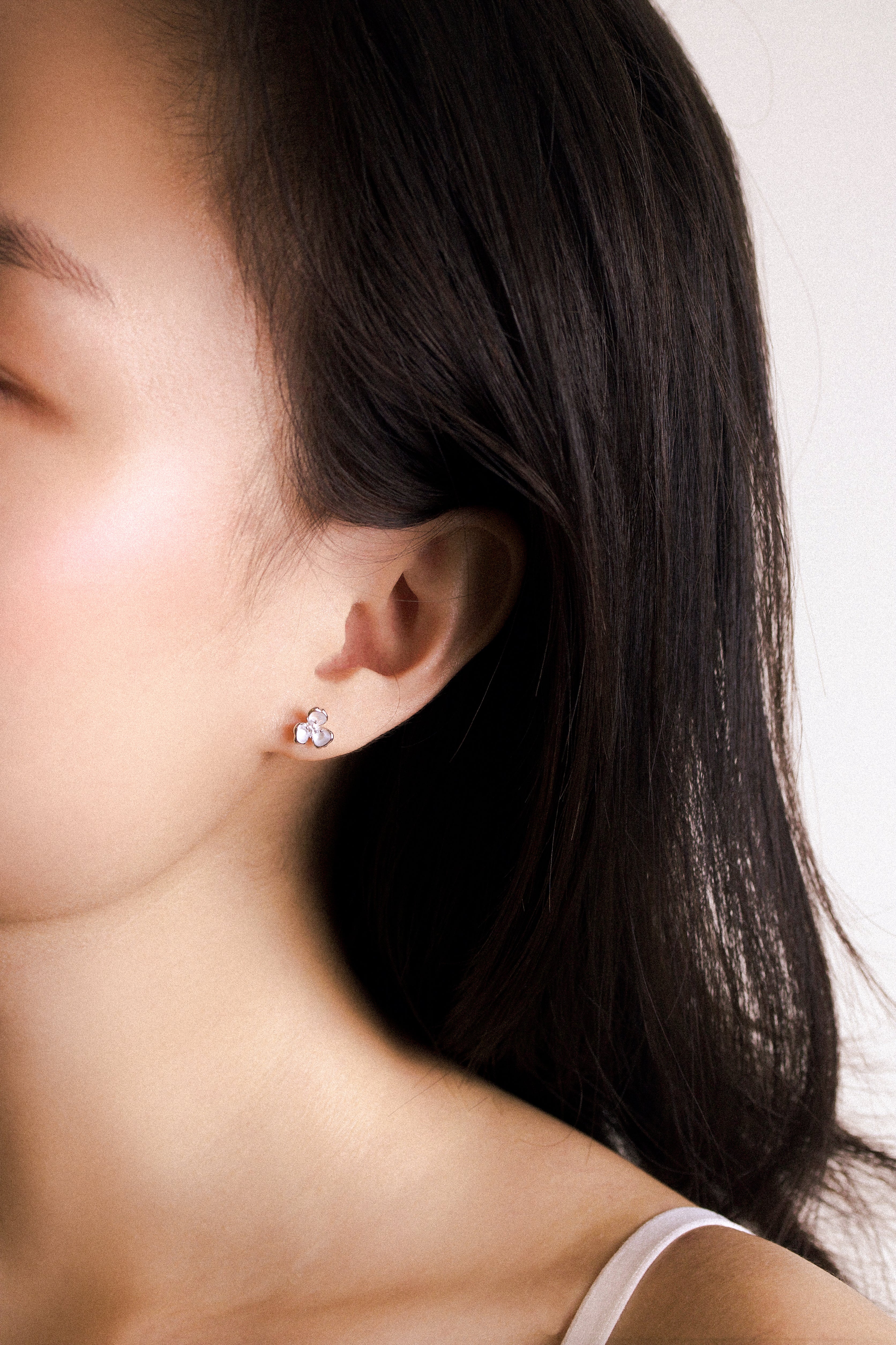 Fine jewellery, silver jewellery, hypoallergenic, tarnish-free, zoomed out front view of a silver ear studs shaped like flower worn on a person's ear