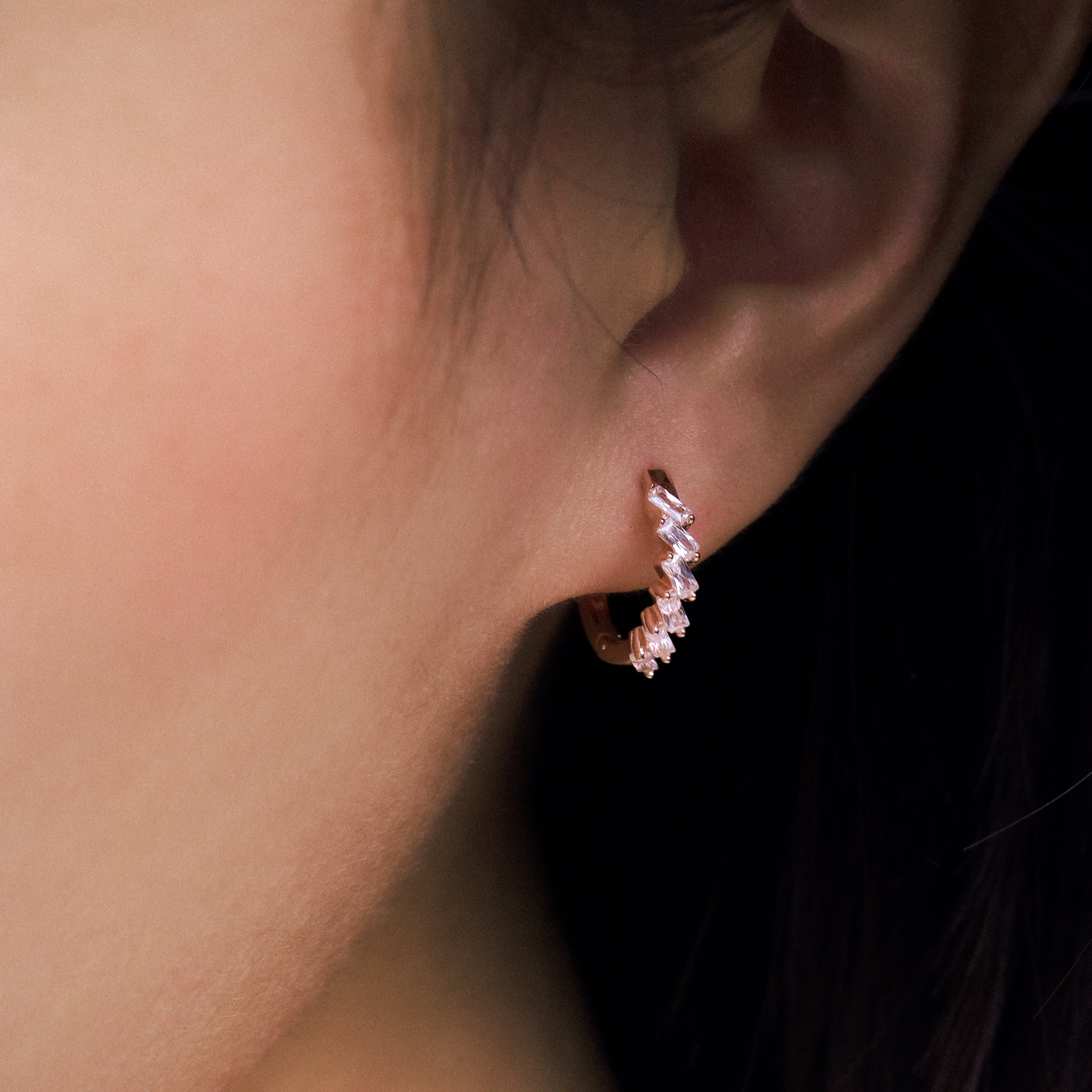 Fine jewellery, silver jewellery plated with rose gold, hypoallergenic, tarnish-free, Close-up front view of an ear wearing a small crystal hoop earring with a dark background