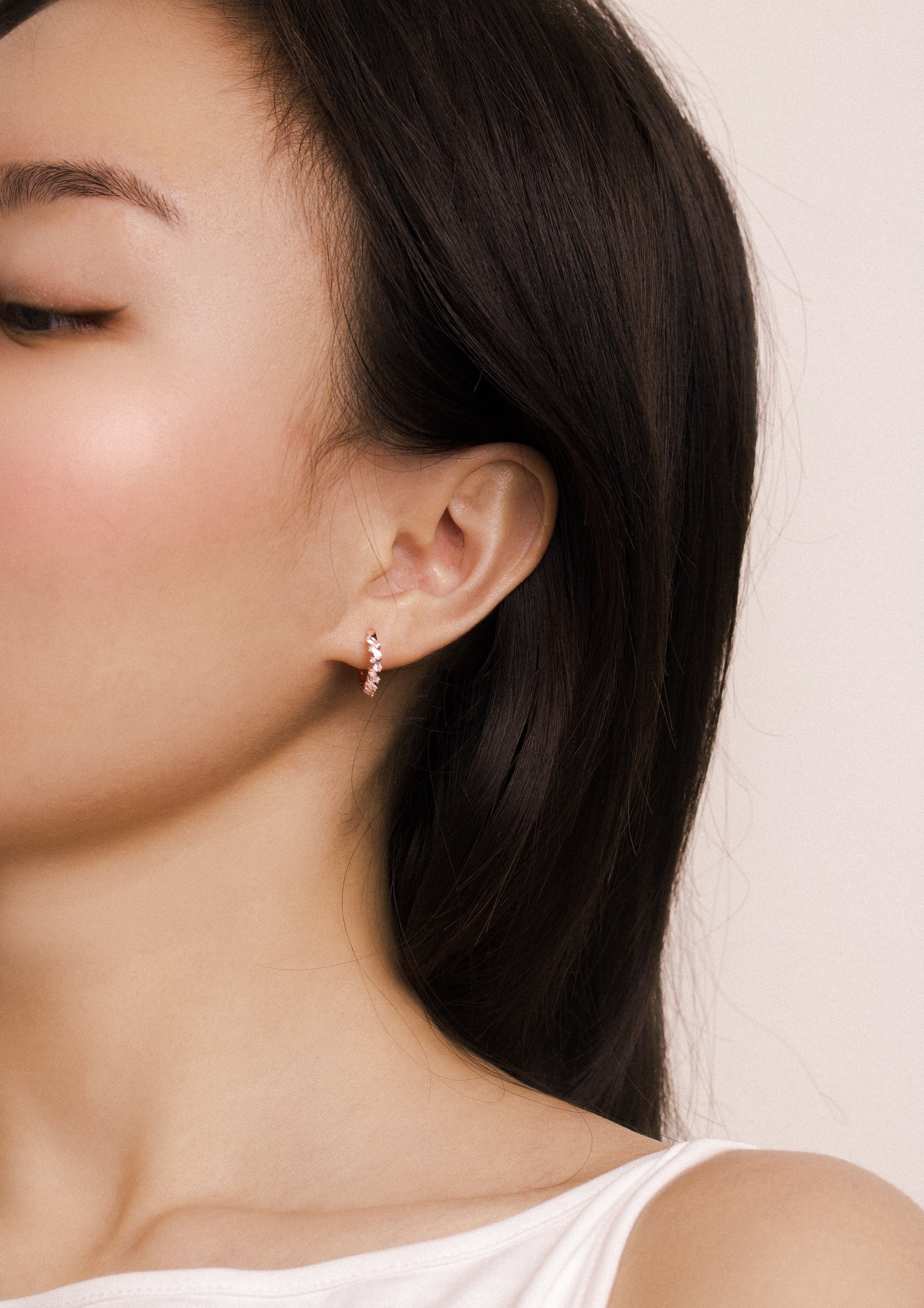 Fine jewellery, silver jewellery plated with rose gold, hypoallergenic, tarnish-free, full front view of a woman wearing a small crystal earring with a neutral background
