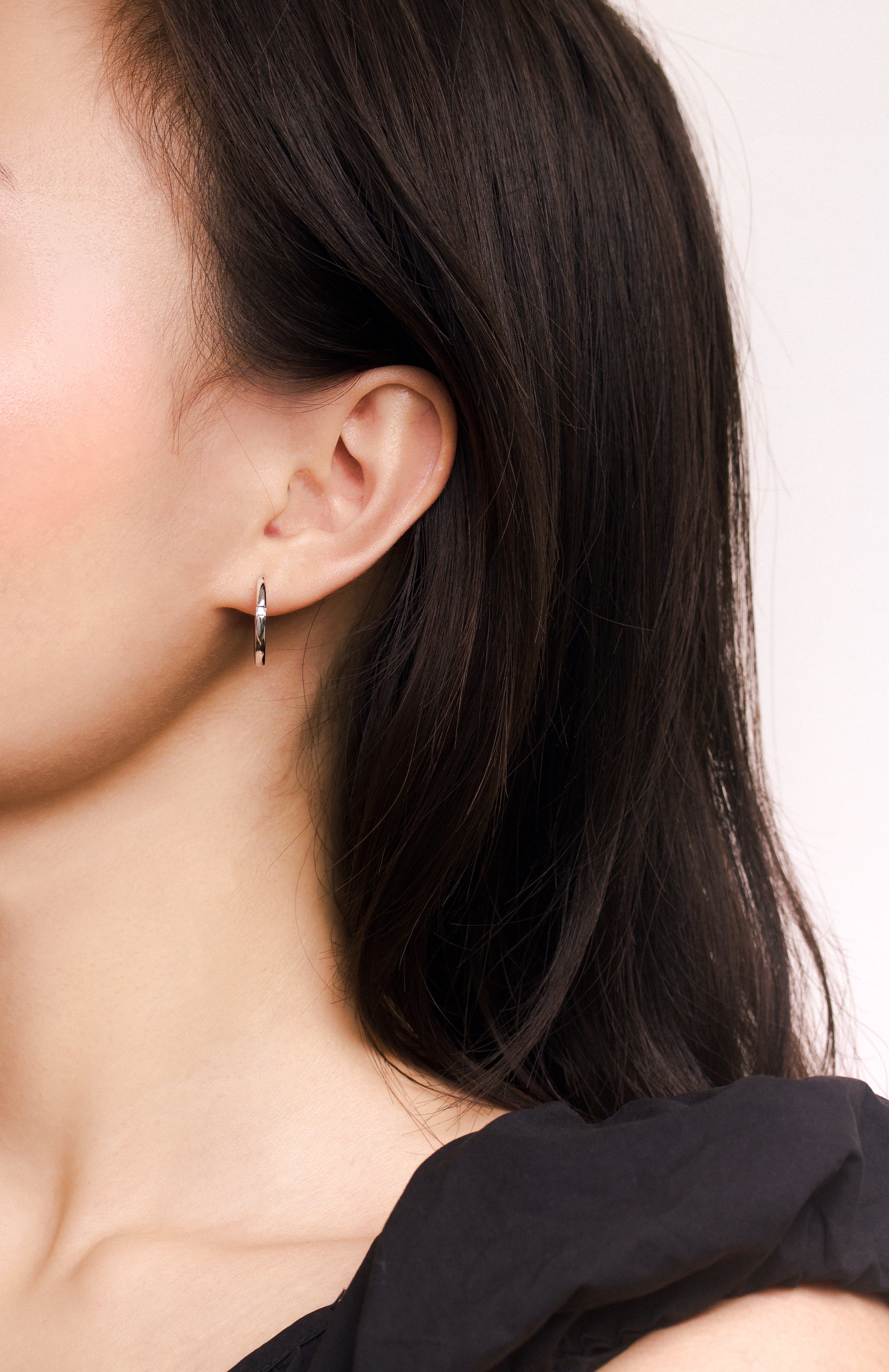 Fine jewellery, silver jewellery, hypoallergenic, tarnish-free, full front view  of a person wearing a silver hoop earring with a neutral background