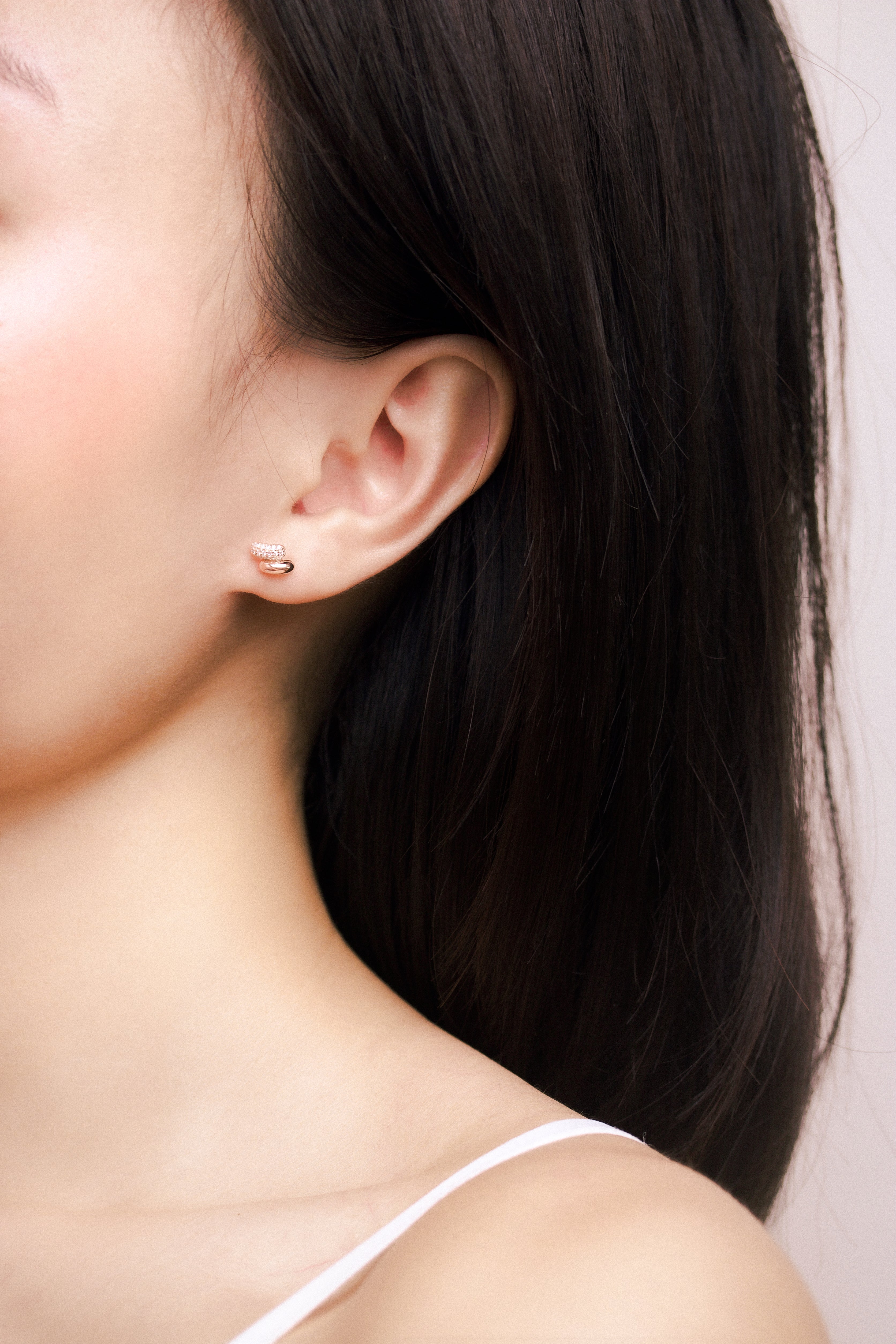 Fine jewellery, silver jewellery plated with rose gold, hypoallergenic, tarnish-free, zoomed out front view of a rose gold earrings embedded with crystals worn on a person's ear
