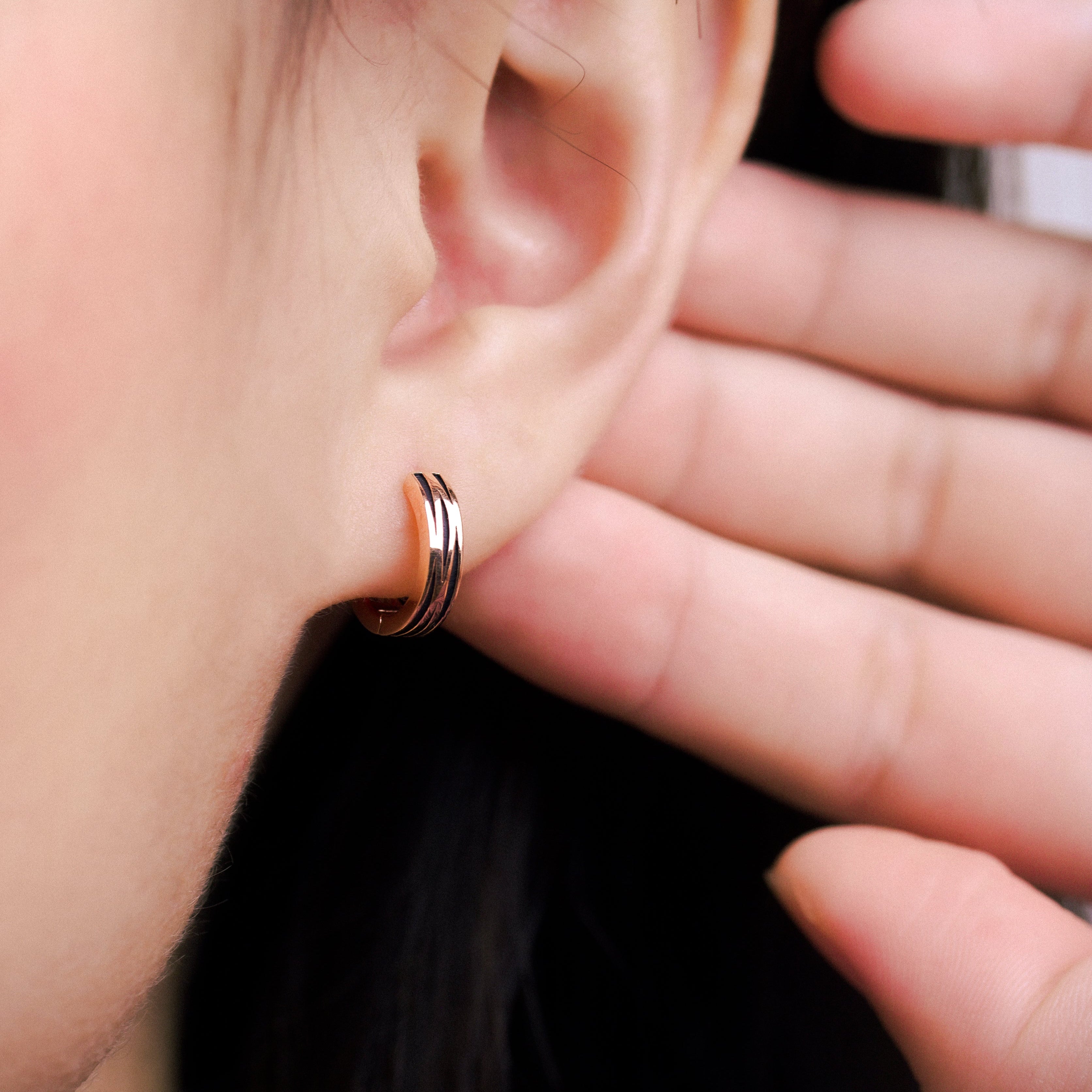 Fine jewellery, silver jewellery, hypoallergenic, tarnish-free, close-up right view of a pair of Rose gold hoop earrings with glazed black stripes worn on a person's ear