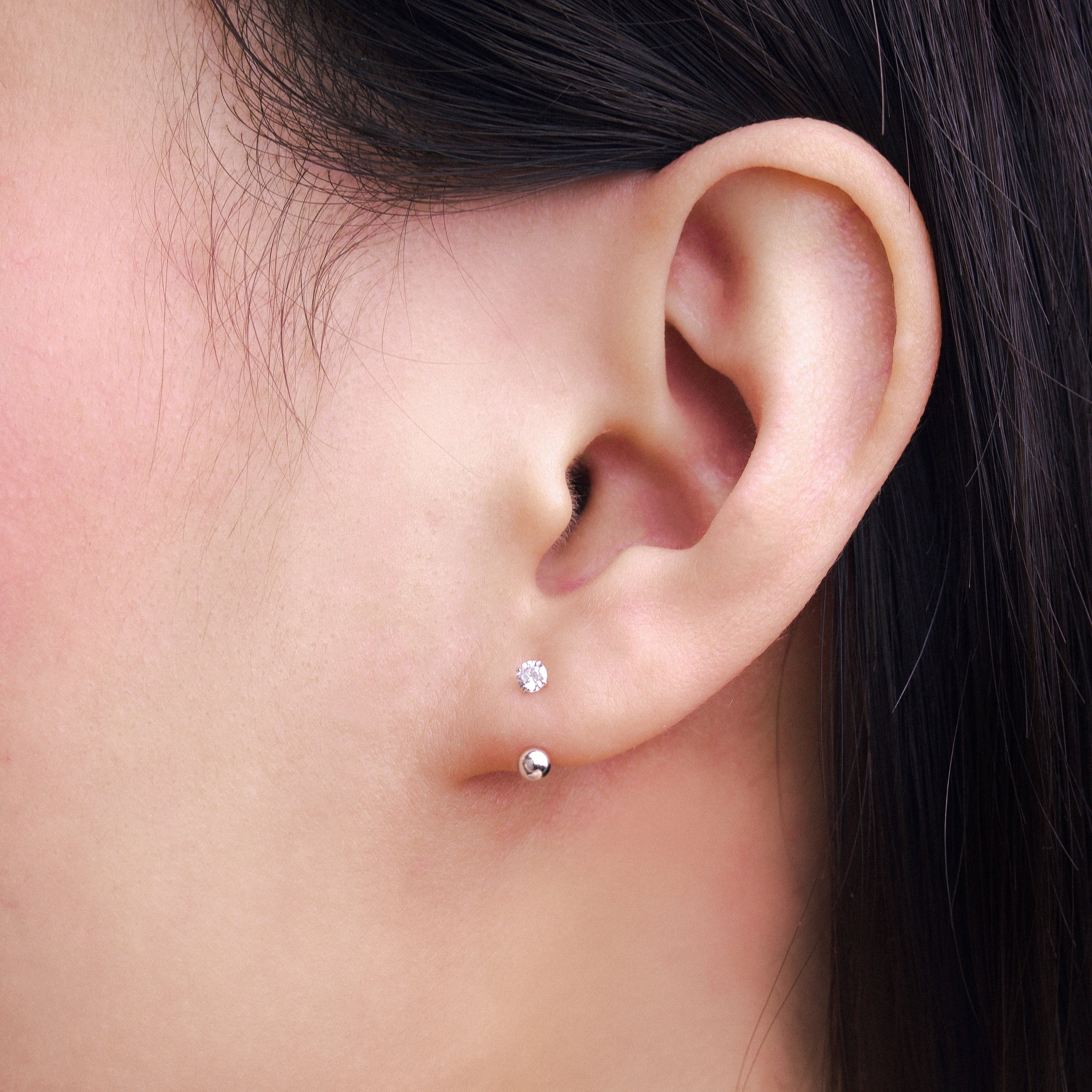 Fine jewellery, silver jewellery, hypoallergenic, tarnish-free, side view Close-up of an ear with small stud earrings with crystal and a silver spherical end.