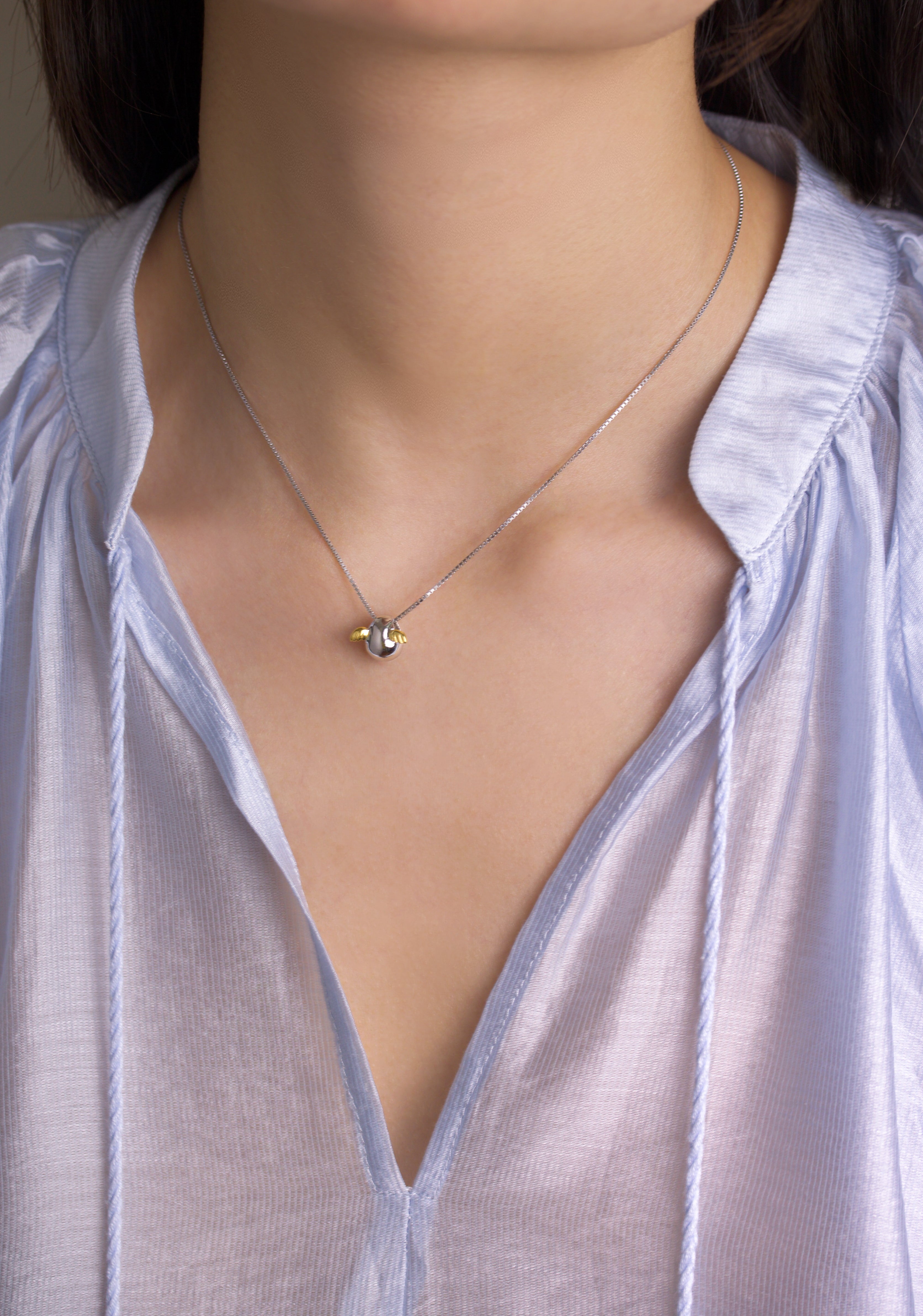 Fine jewellery, silver jewellery, hypoallergenic, tarnish-free, full view of silver Necklace with a small pendant with golden wings worn by a person in a light blue shirt.