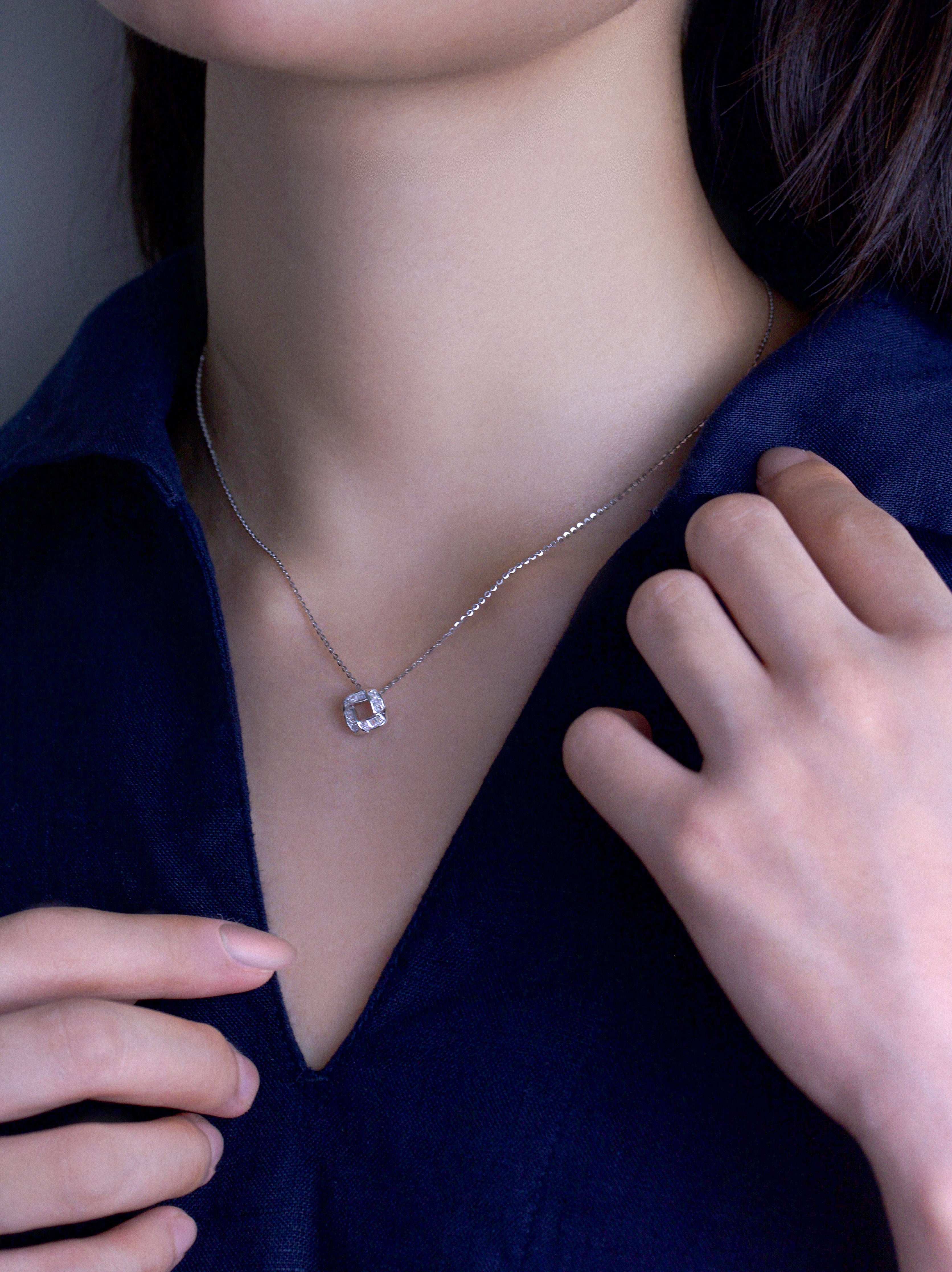 Fine jewellery, silver jewellery, hypoallergenic, tarnish-free, side view of a  necklace with a diamond pendant worn on a person with dark blue shirt touching their collarbone.