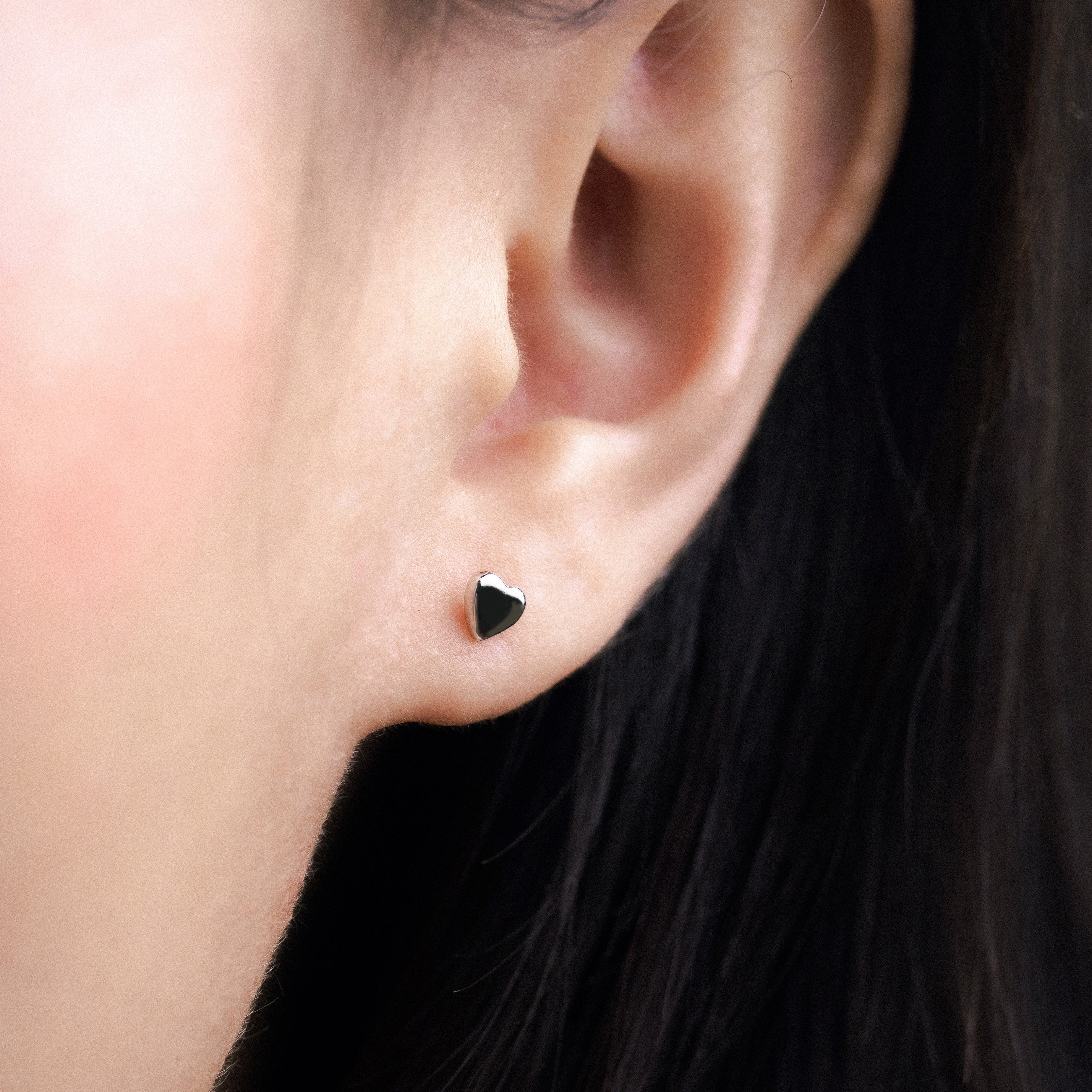 Fine jewellery, silver jewellery, hypoallergenic, tarnish-free, Close up side view of a pair of Heart-shaped silver ear studs worn by a person