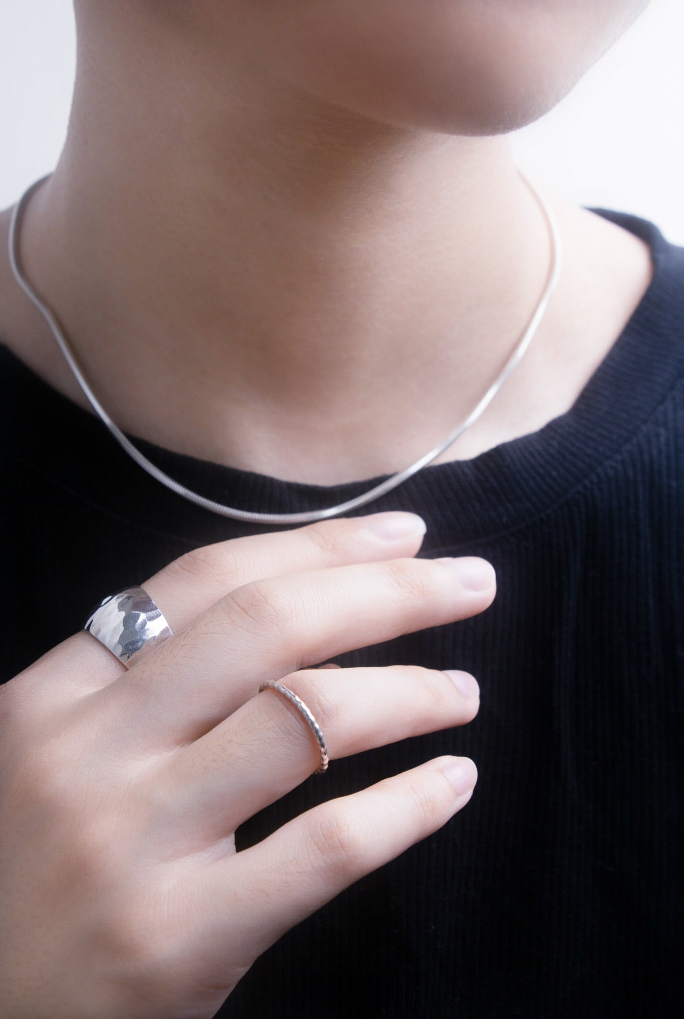 Close-up front view of a person wearing a silver necklace and rings on a plain black background
