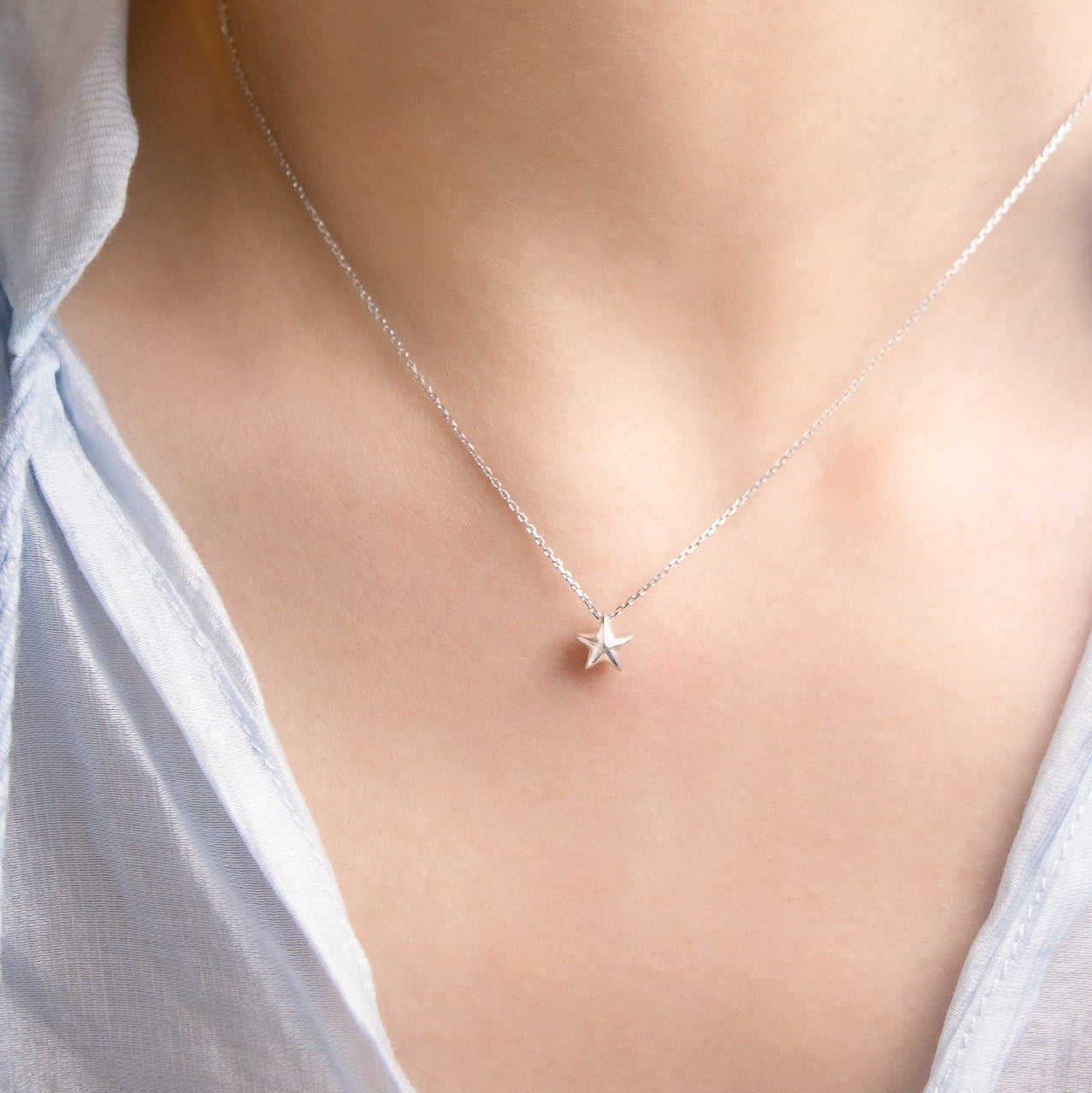 close-up view of a Silver necklace with a star pendant on a person wearing a white shirt.