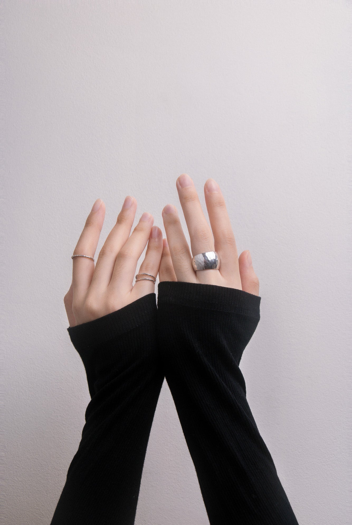 Hands wearing black arm sleeves with silver rings on a plain background, close up front view