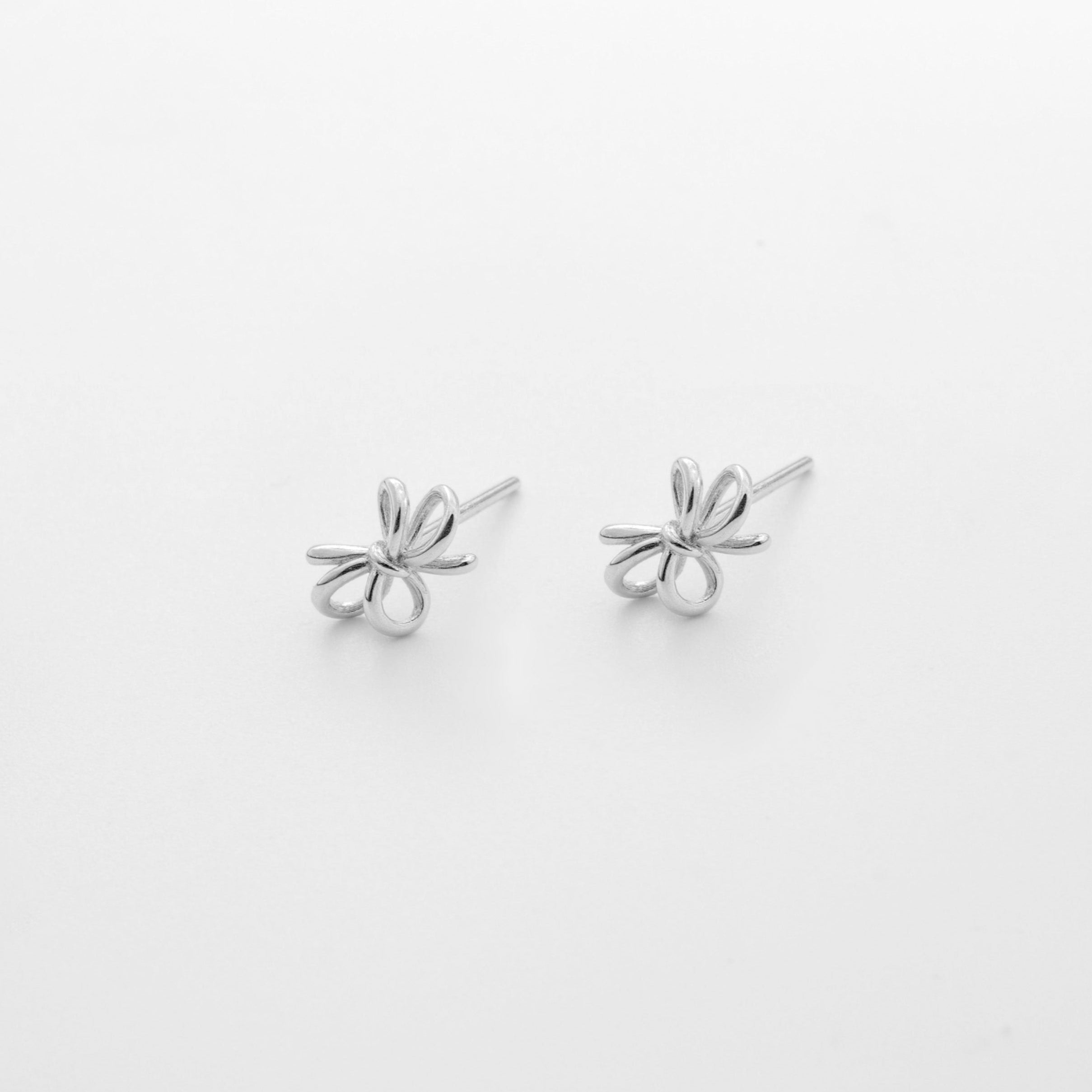 Pair of bow-shaped silver earrings on a light gray background