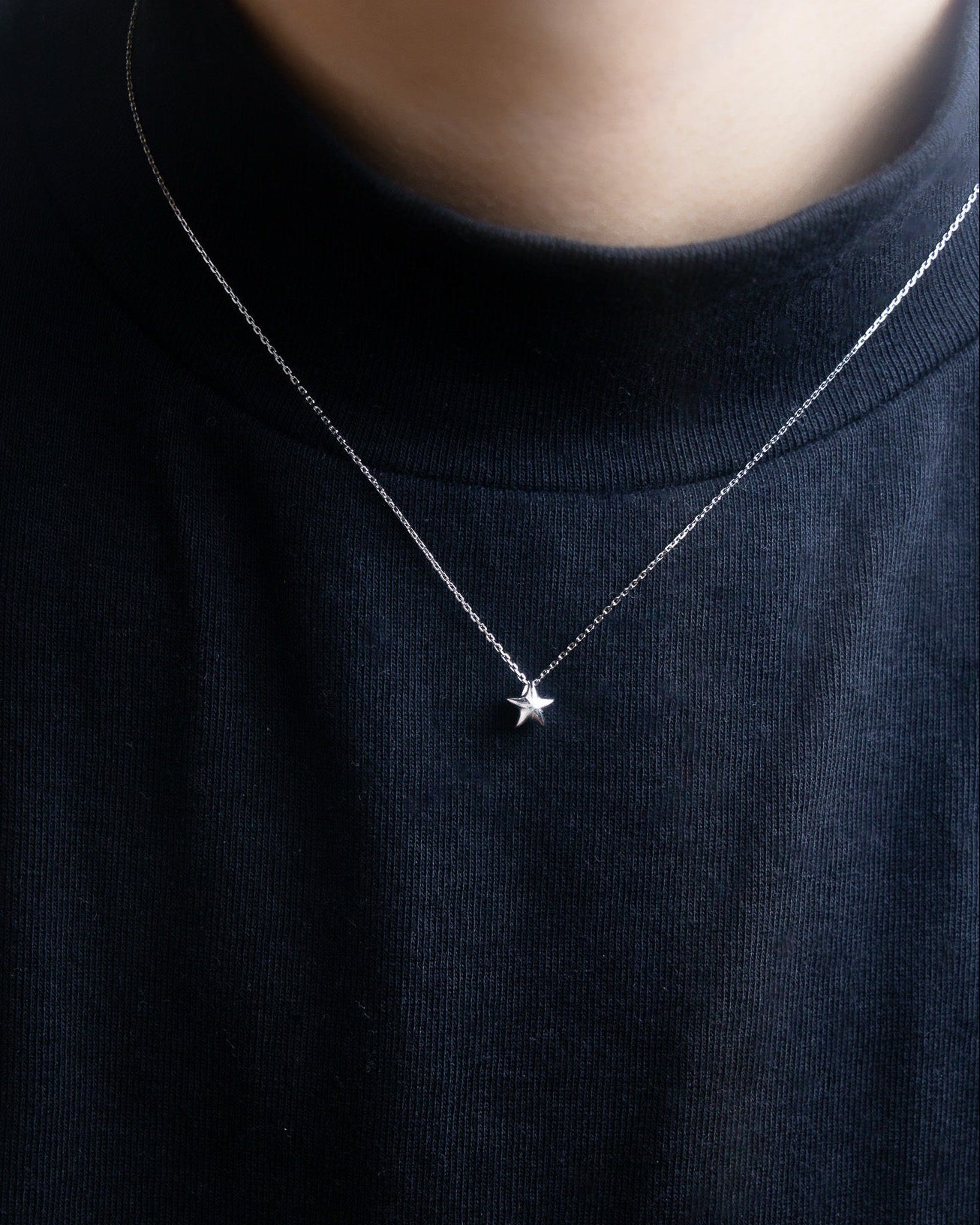 Close-up view of a silver Star-shaped necklace on a person wearing a black shirt