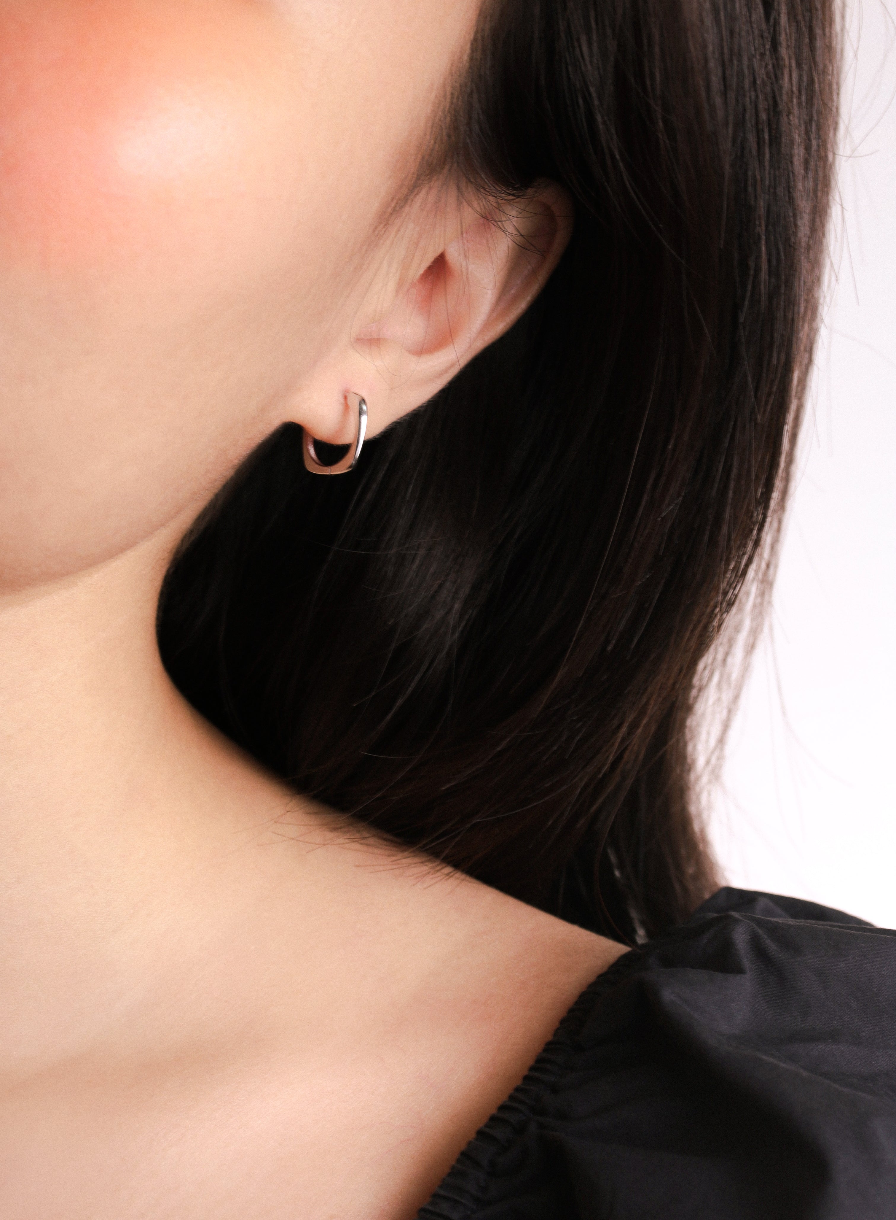 Fine jewellery, silver jewellery, hypoallergenic, tarnish-free, zoomed out left view of a Pair of squarish silver hoop earrings worn on a person's ear