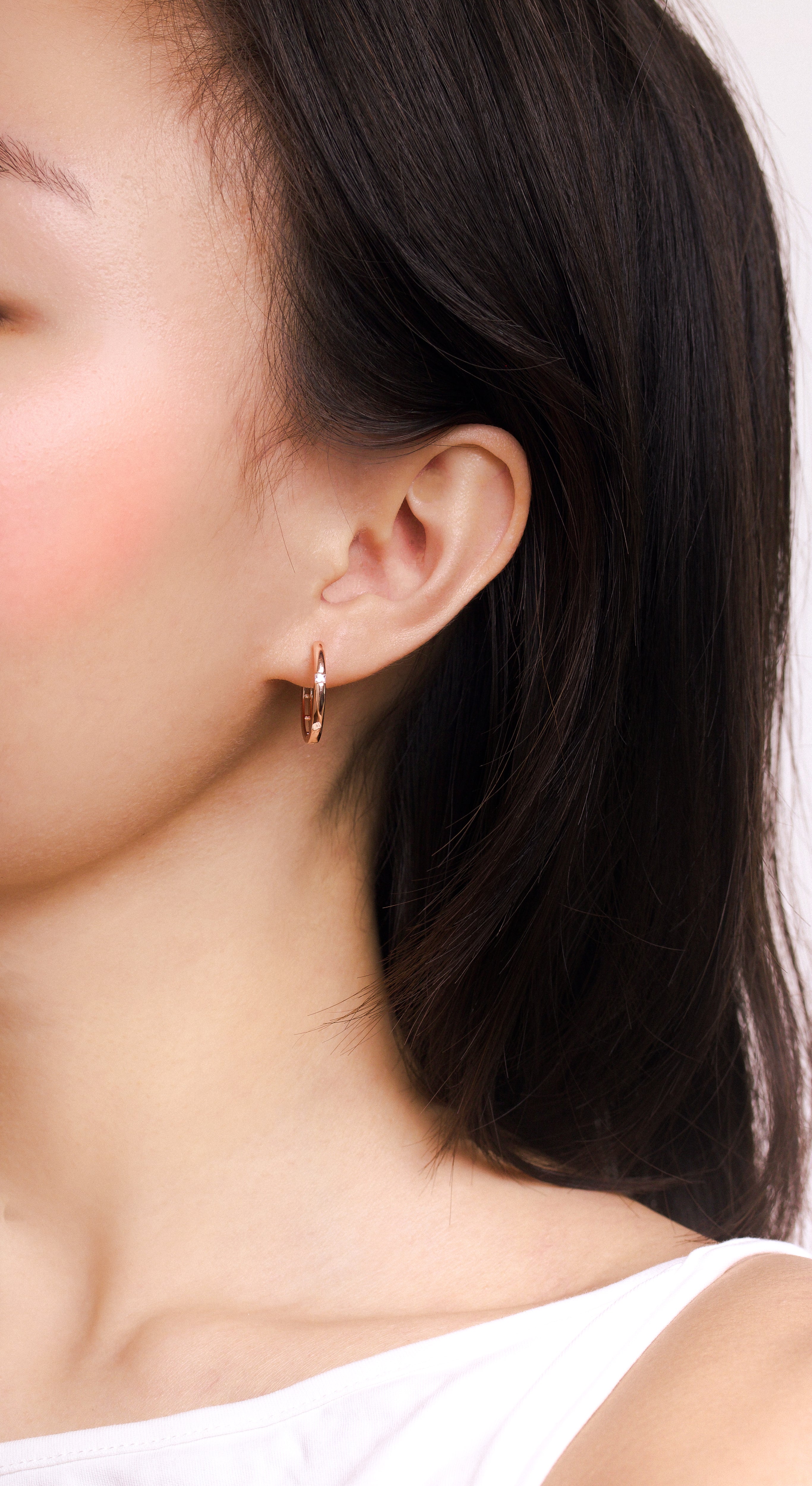 Fine jewellery, silver jewellery plated with rose gold, hypoallergenic, tarnish-free, full front view of a person wearing a rose gold hoop earring with a plain background