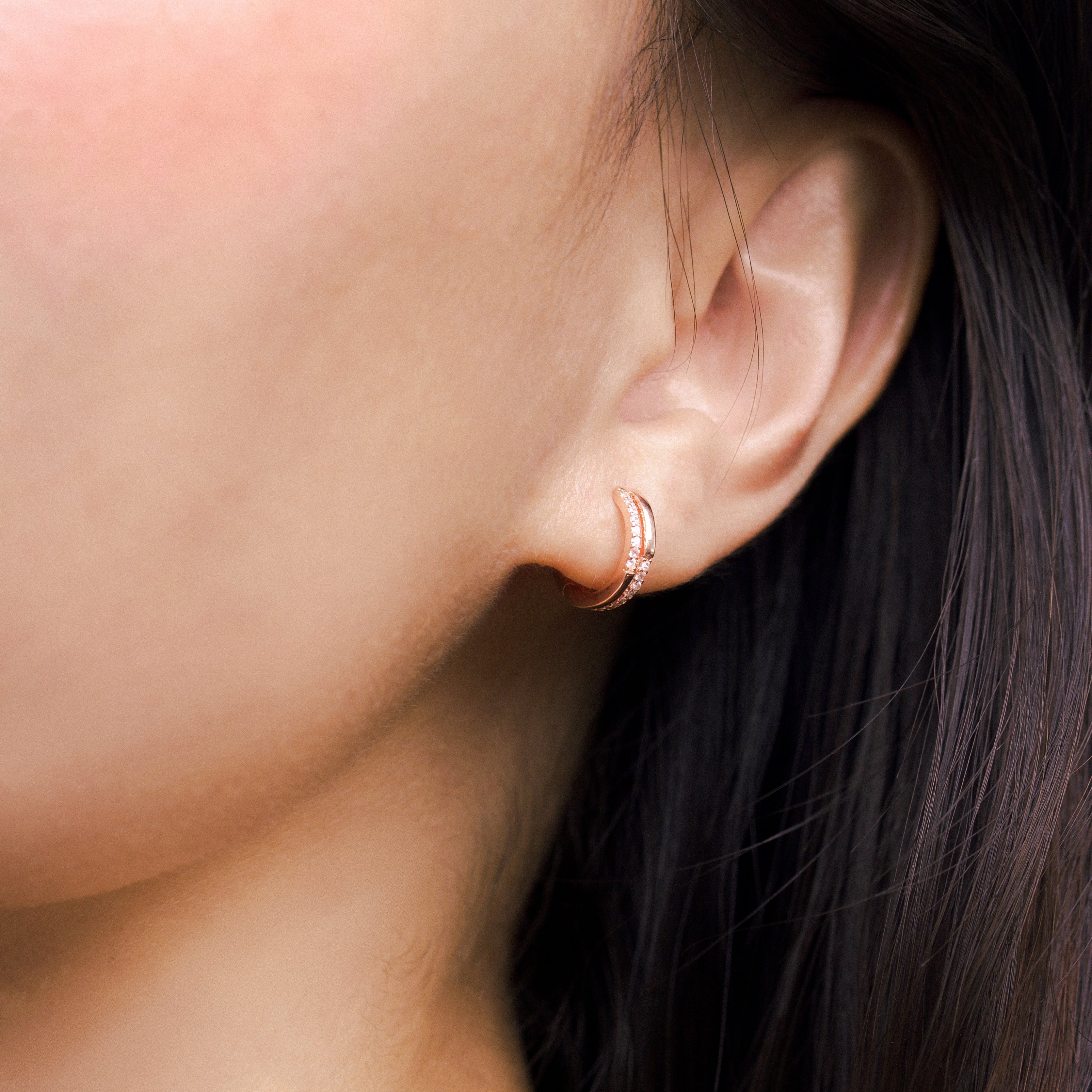Fine jewellery, silver jewellery plated with rose gold, hypoallergenic, tarnish-free, close-up right view of a Rose gold hoop earrings with embedded crystals worn on a person's ear