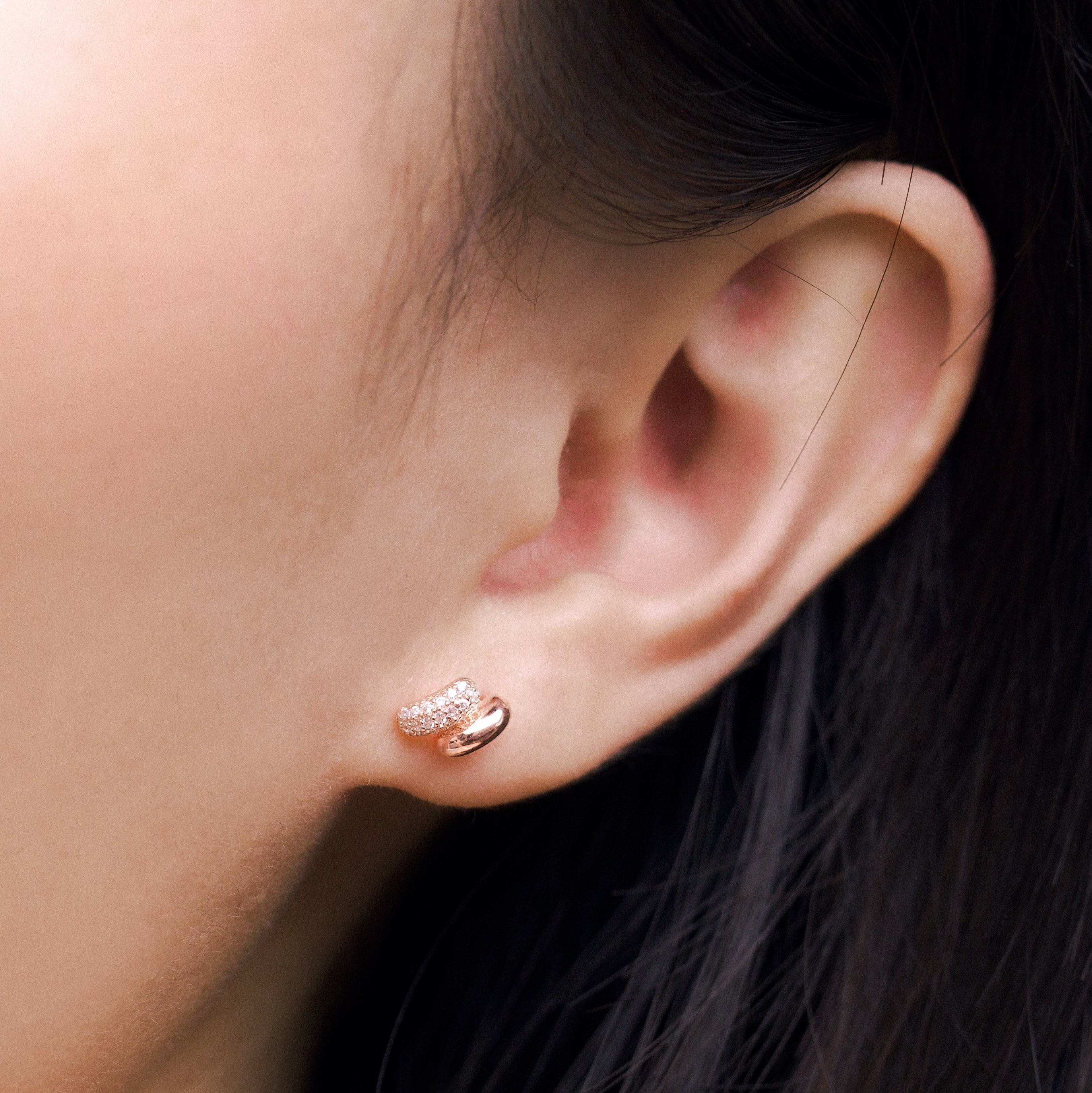 Fine jewellery, silver jewellery plated with rose gold, hypoallergenic, tarnish-free, close-up front view of a rose gold earrings embedded with crystals worn on a person's ear
