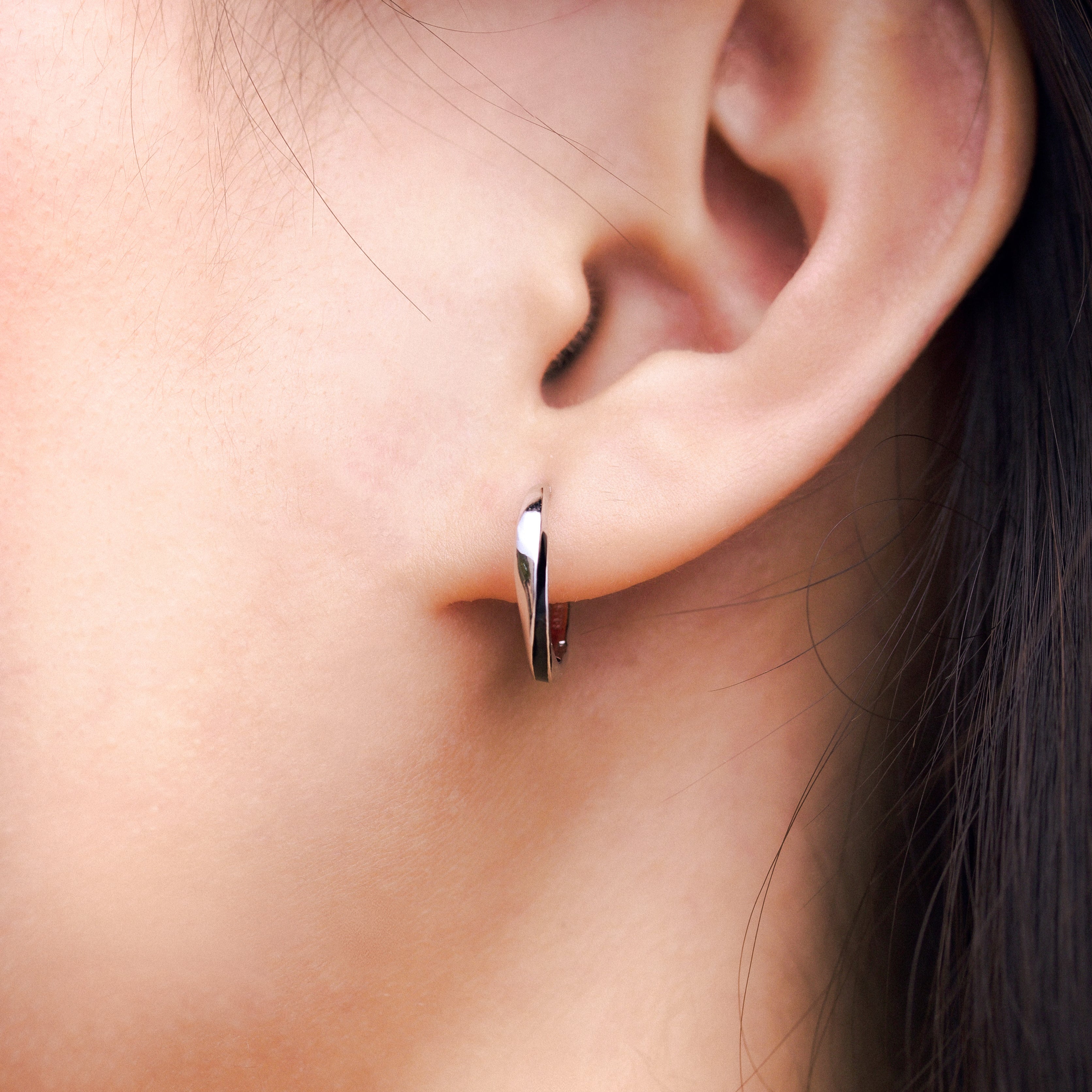 Fine jewellery, silver jewellery, hypoallergenic, tarnish-free, close-up front view of a Pair of silver glazed black hoop earrings worn on a person's ear