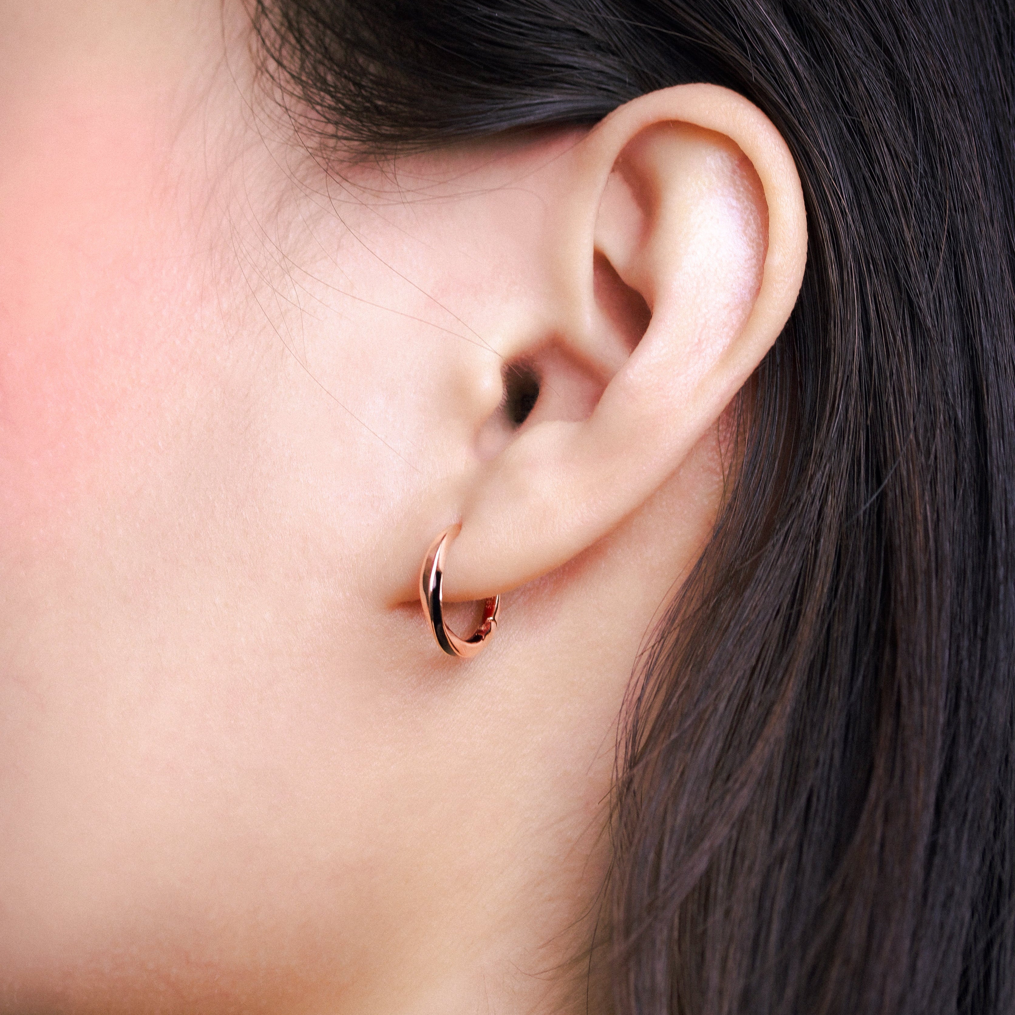 Fine jewellery, silver jewellery plated with rose gold, hypoallergenic, tarnish-free, close-up left view of a Rose gold glazed black hoop earrings worn on a person's ear