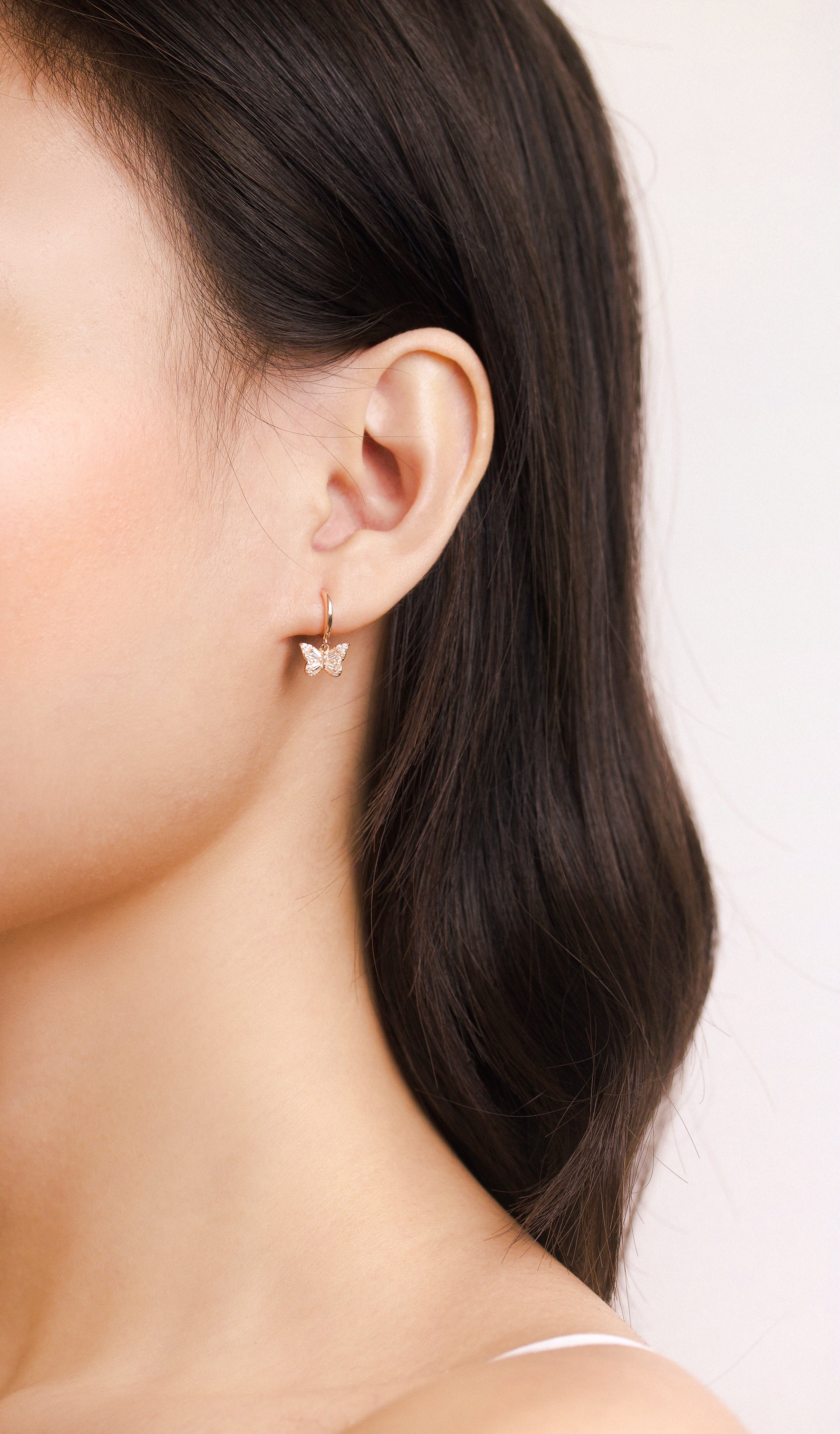 Fine jewellery, silver jewellery plated with rose gold, hypoallergenic, tarnish-free, full front view of a person wearing a butterfly-shaped earring with a plain background