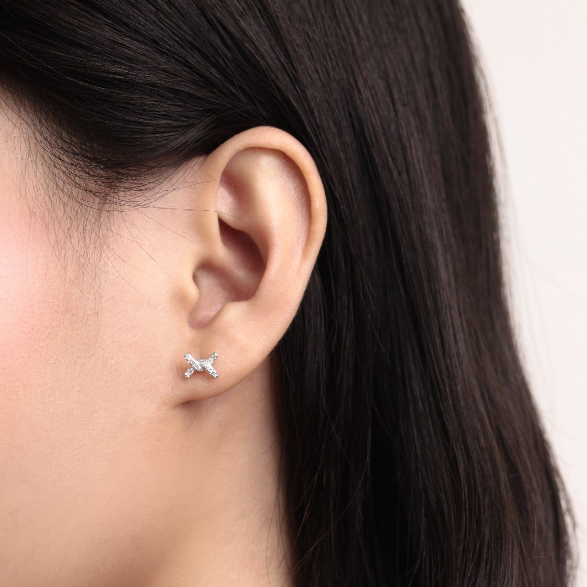 Fine jewellery, silver jewellery, hypoallergenic, tarnish-free, close-up side view of Pair of silver 'X' shaped like a ribbon knot earrings with crystal worn on a person's ear