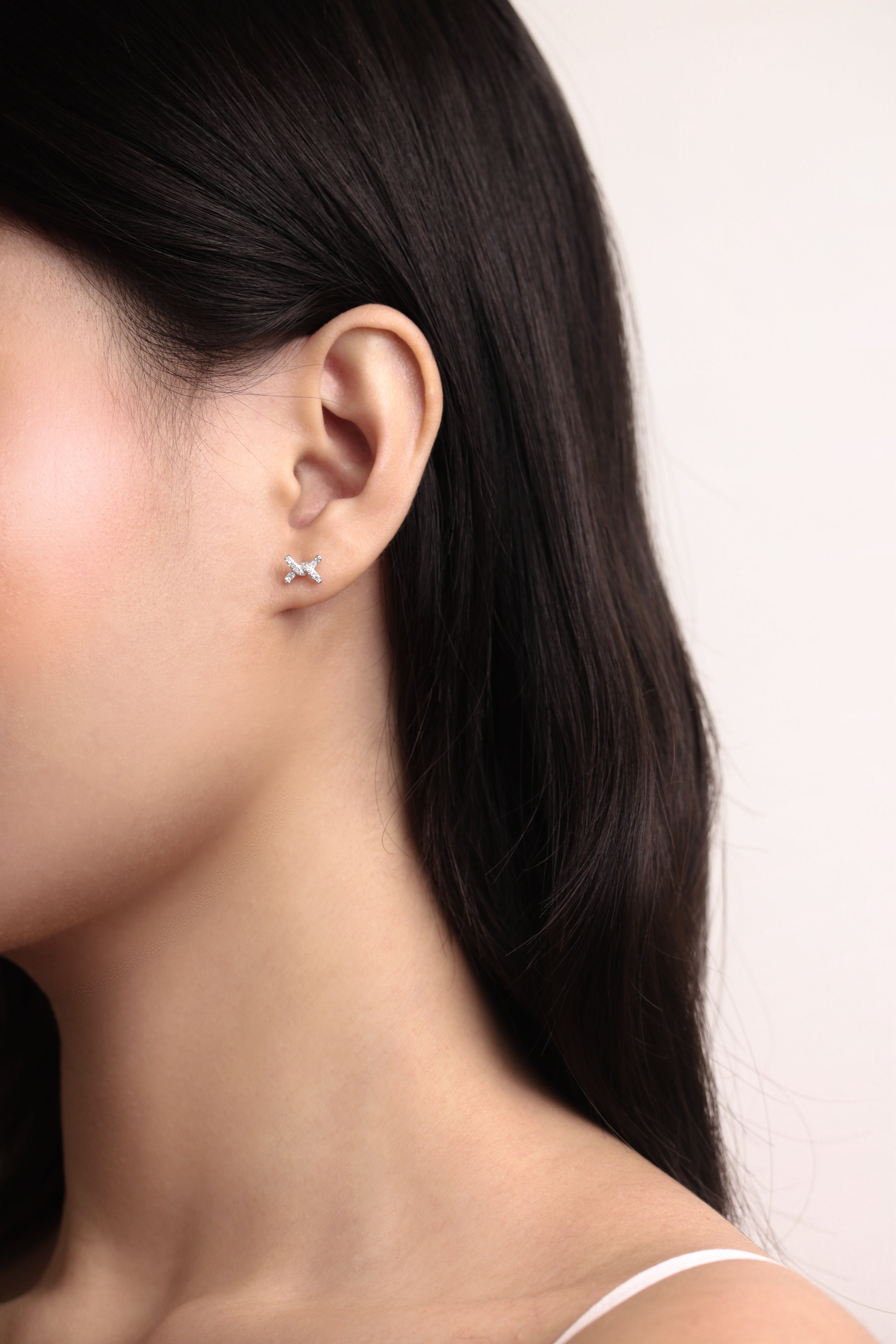 Fine jewellery, silver jewellery, hypoallergenic, tarnish-free, side full  view of Pair of silver 'X' shaped like a ribbon knot earrings with crystal worn on a person's ear