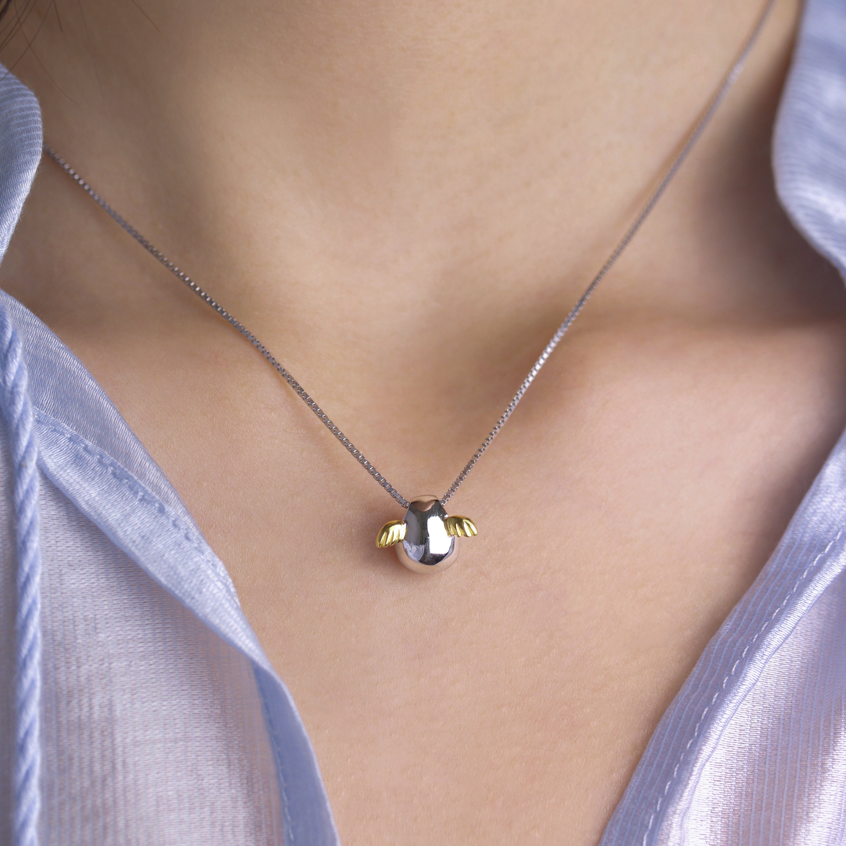 Fine jewellery, silver jewellery, hypoallergenic, tarnish-free, front view close-up of silver Necklace with a small pendant with golden wings worn by a person on the neck