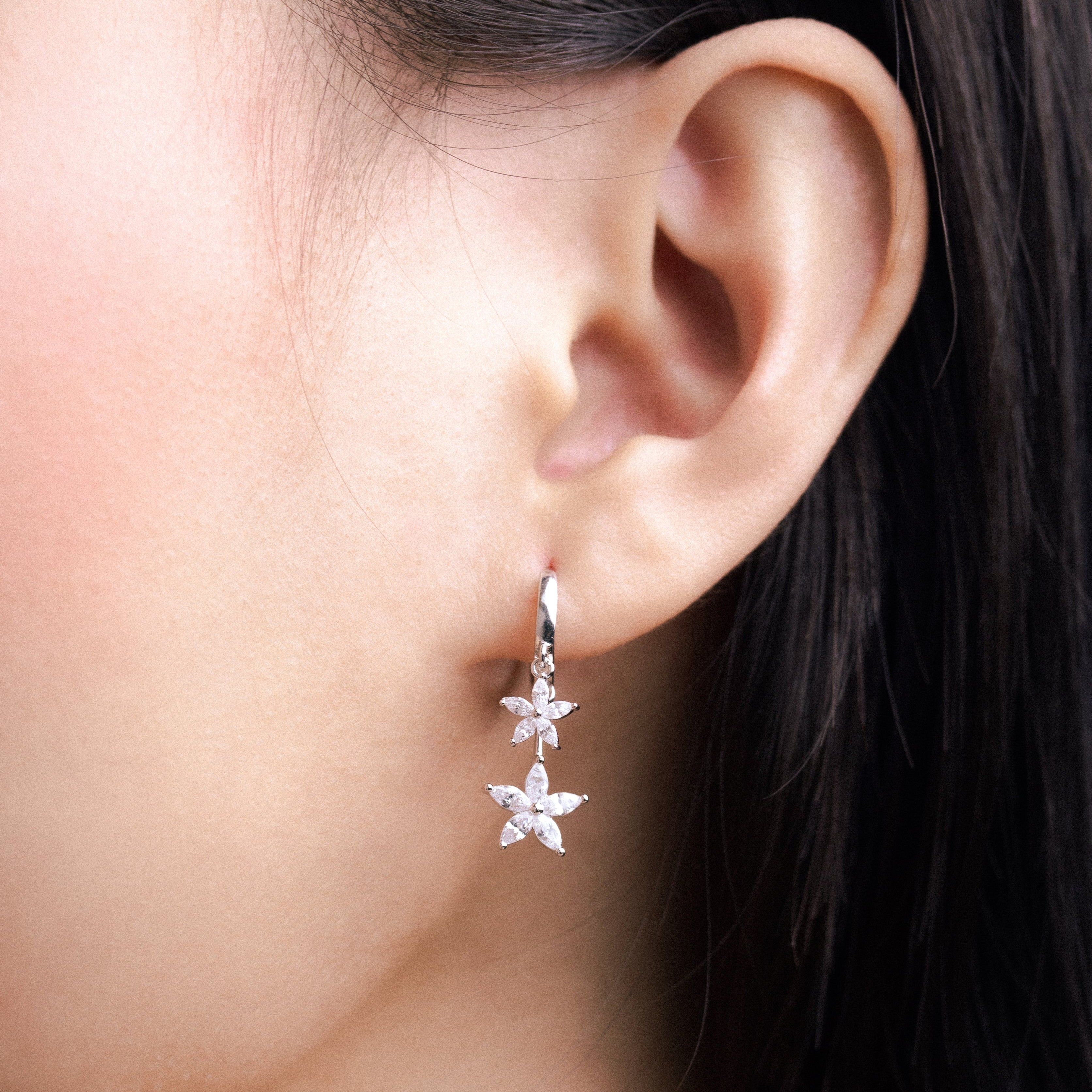 Fine jewellery, silver jewellery, hypoallergenic, tarnish-free,
Close-up front view of a ear wearing a silver flower-shaped adorned with crystal earring
